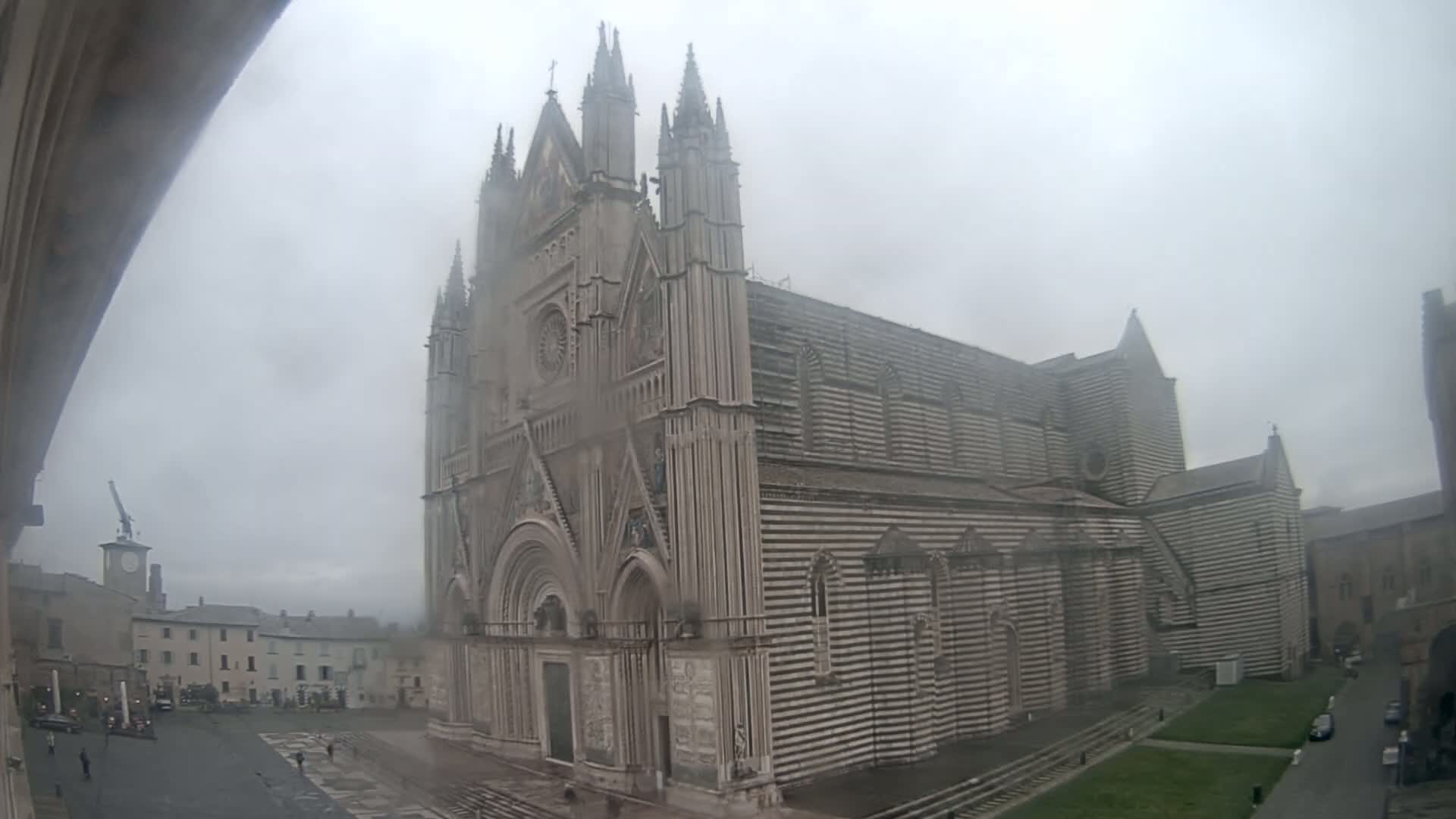 A large, striped stone cathedral stands in a town square on an overcast day.