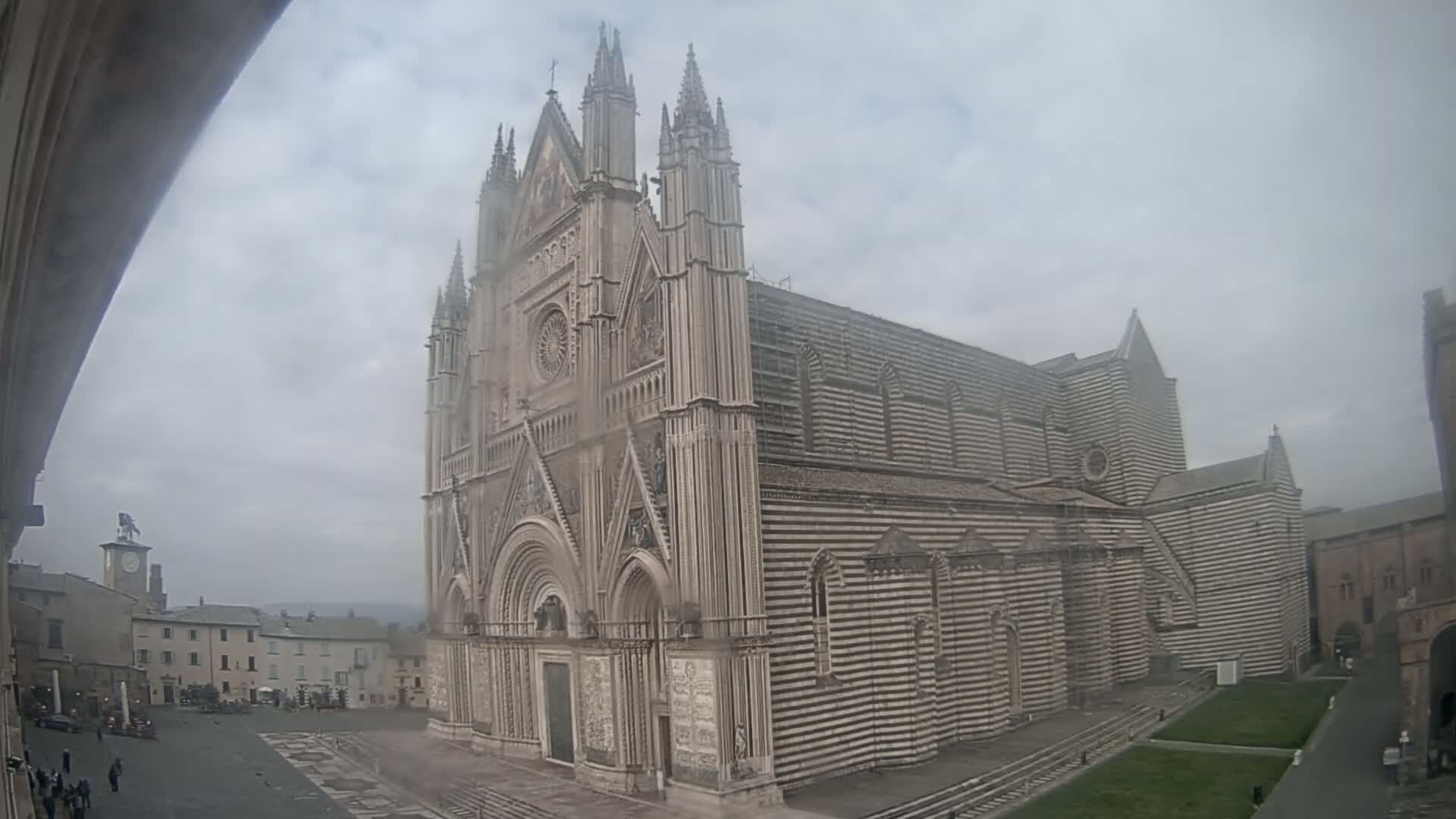 A large striped stone cathedral stands in a town square on an overcast day.