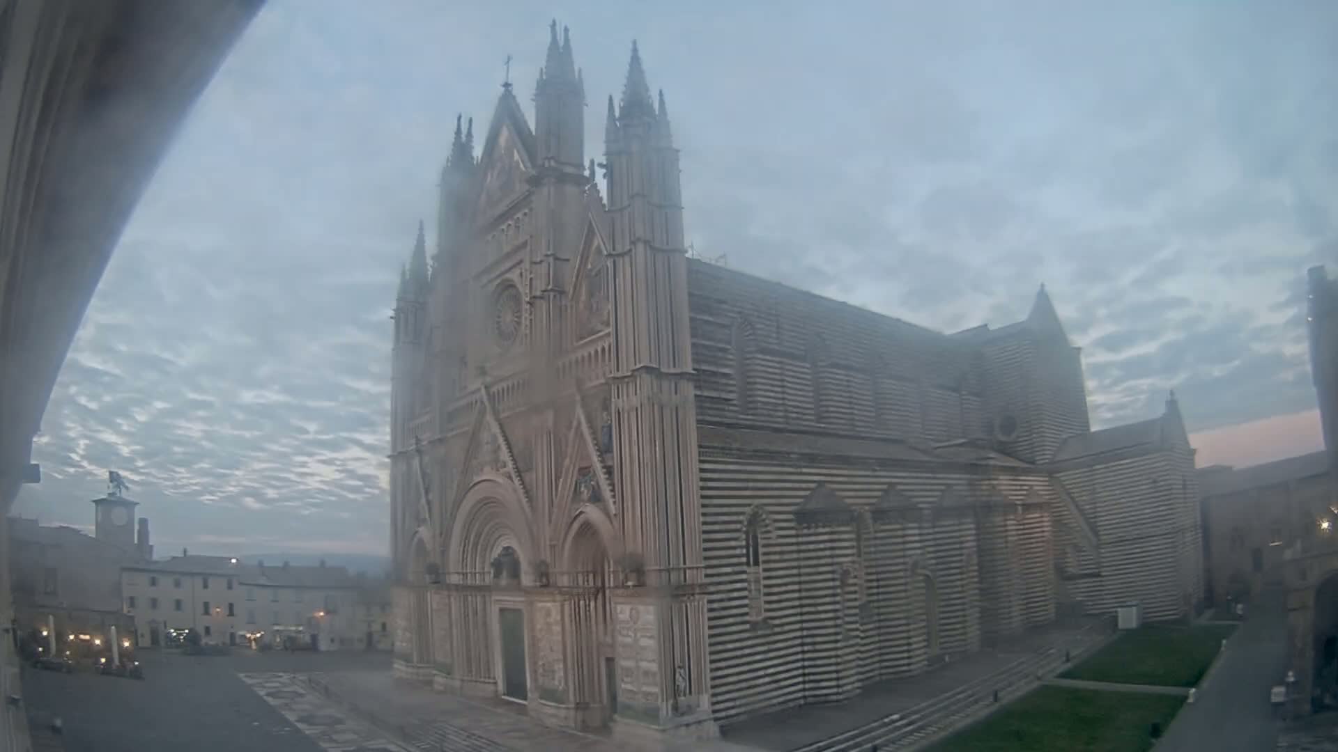 A large, striped cathedral stands in a town square on a foggy, overcast day.