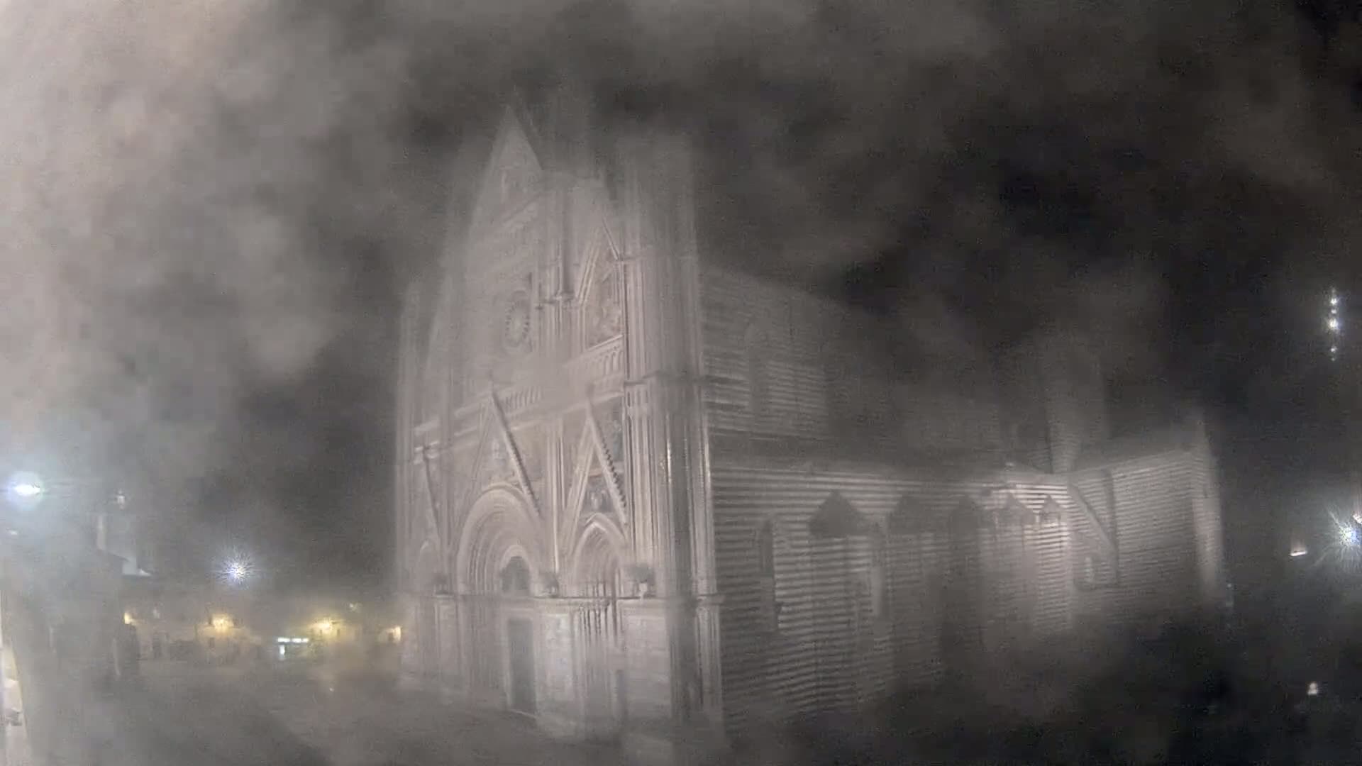 A large stone building, possibly a cathedral, is shrouded in a thick fog at night.