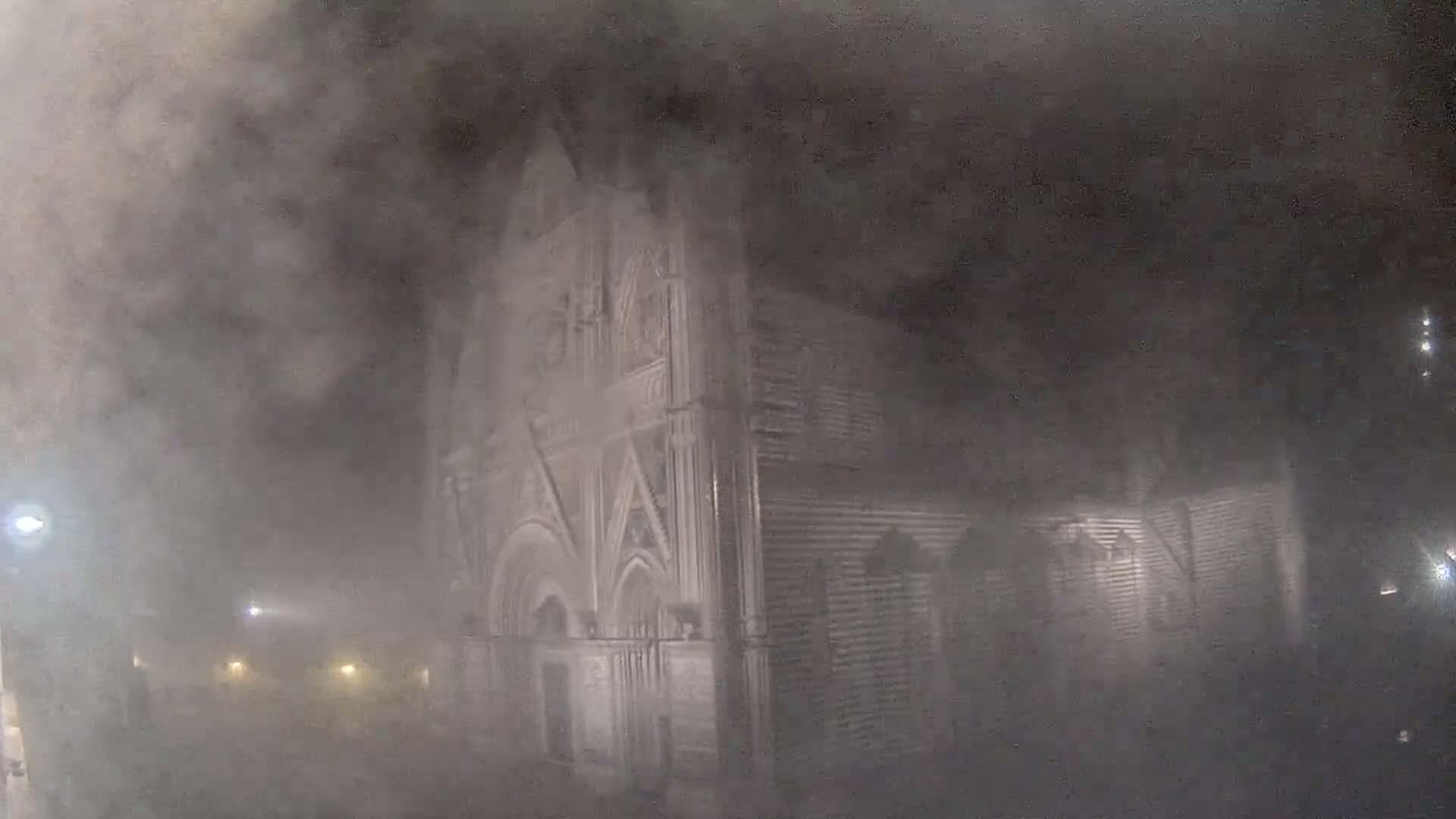 A large stone building, possibly a church, is partially obscured by heavy fog or mist at night.