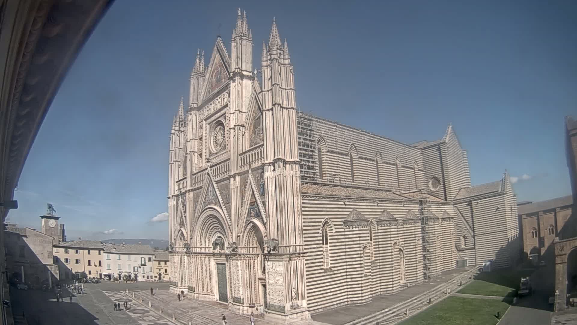 A large, striped cathedral stands in a town square on a sunny day.