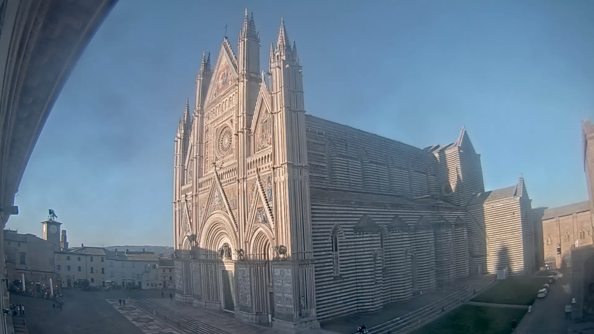 A large, ornate cathedral with black and white striped exterior walls stands in a town square on a clear, sunny day.