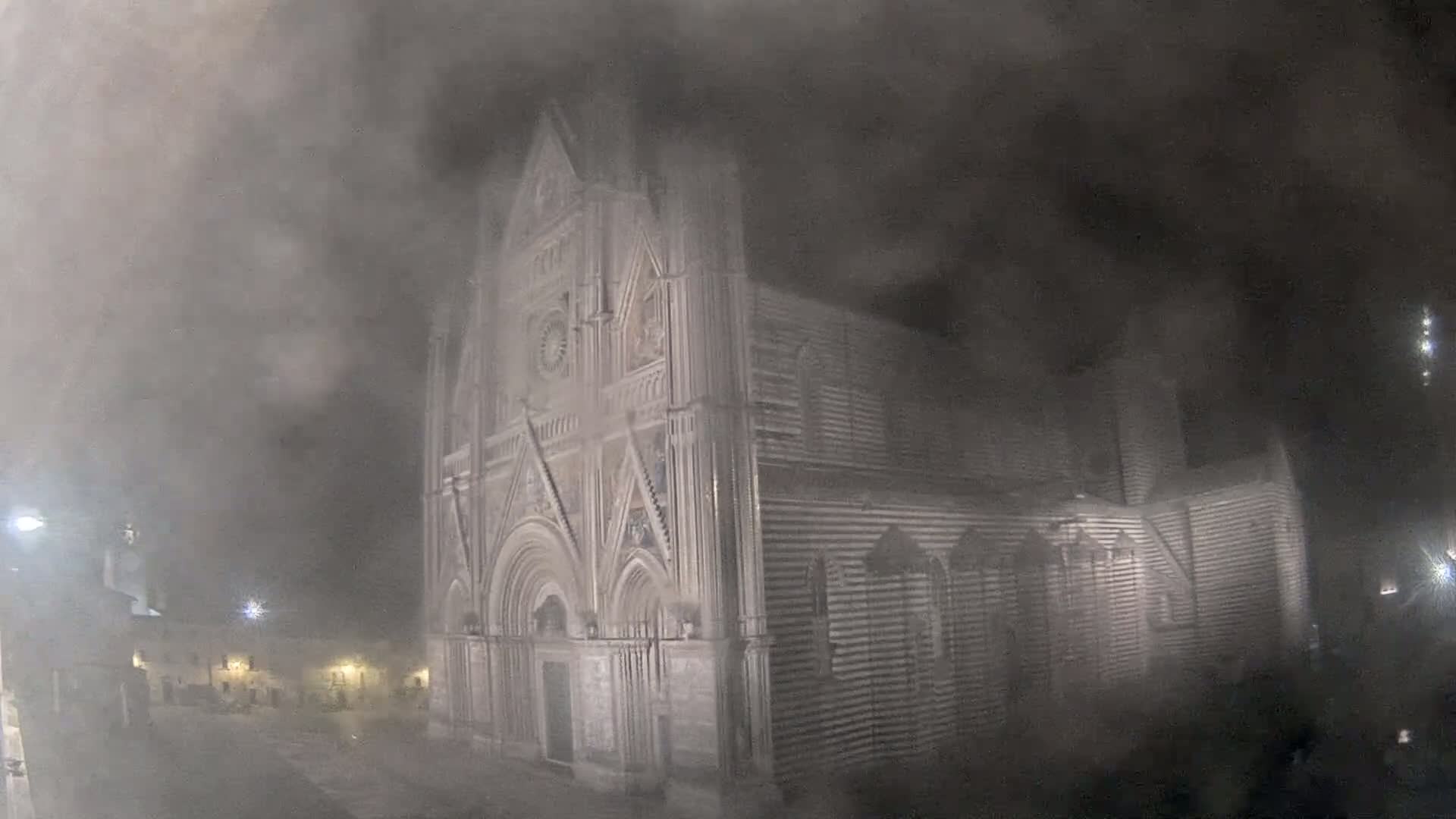 A large stone cathedral is shrouded in heavy fog at night.