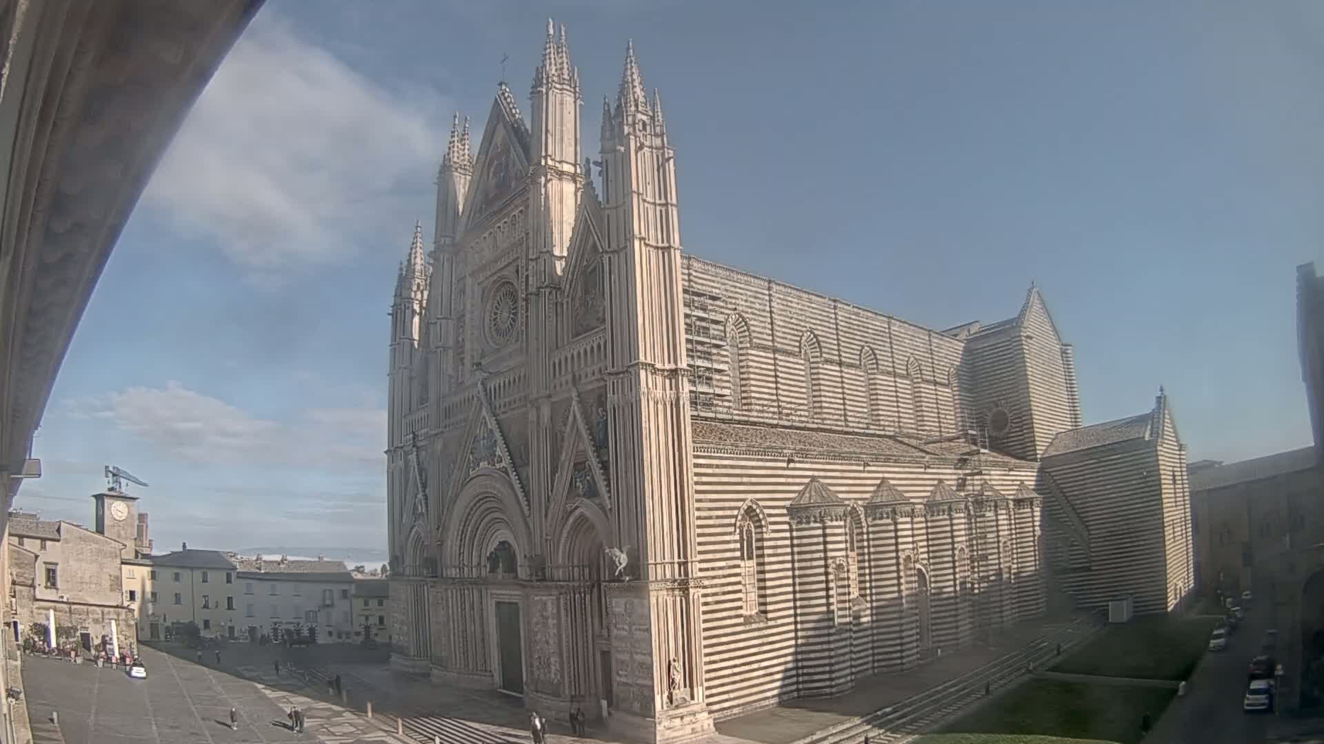 A large, striped cathedral stands in a town square on a partly sunny day.