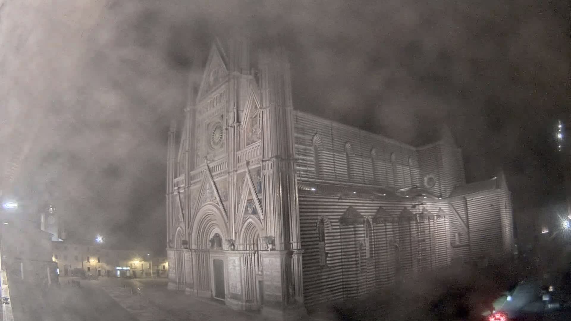 A large, striped stone cathedral is partially obscured by fog at night.