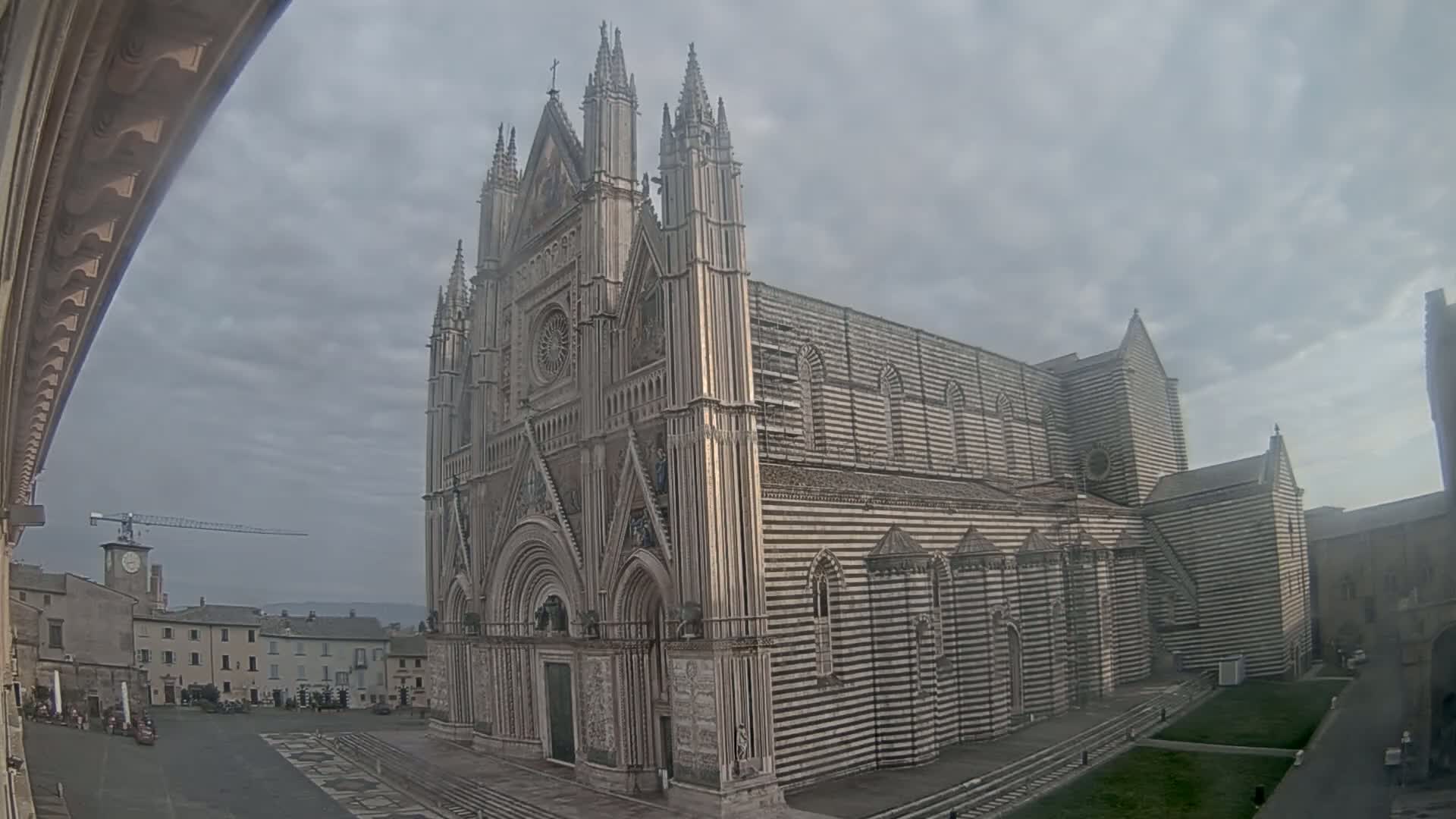 A large, striped cathedral stands in a town square under a cloudy sky.