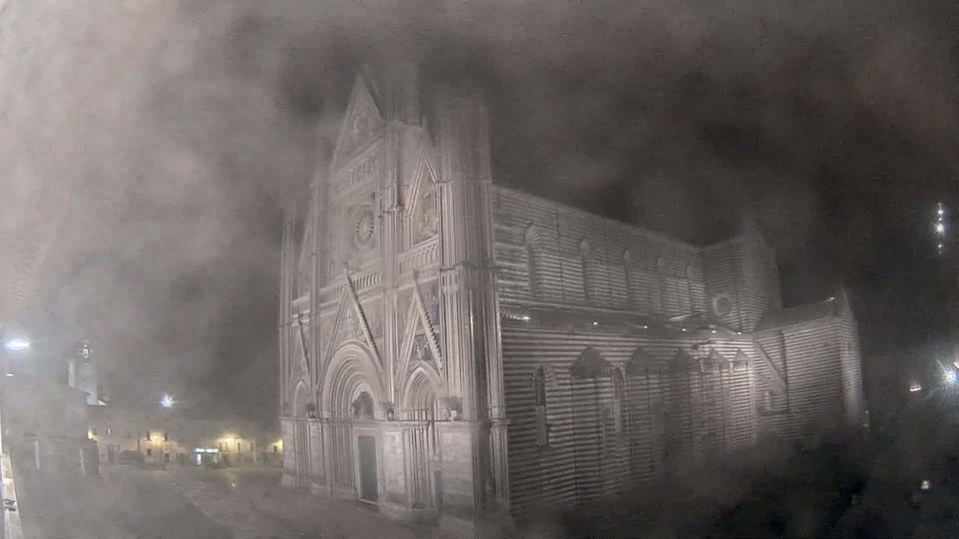 A large, striped stone cathedral stands at night in a heavy fog.