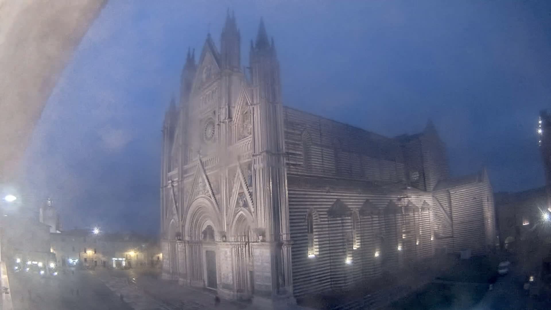 A large, striped cathedral stands in a town square shrouded in fog at night.