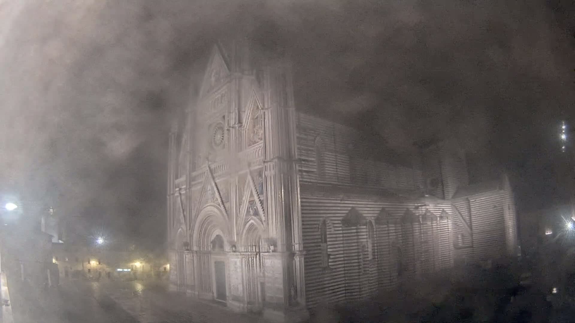 A large, striped stone cathedral is shrouded in a thick fog at night.