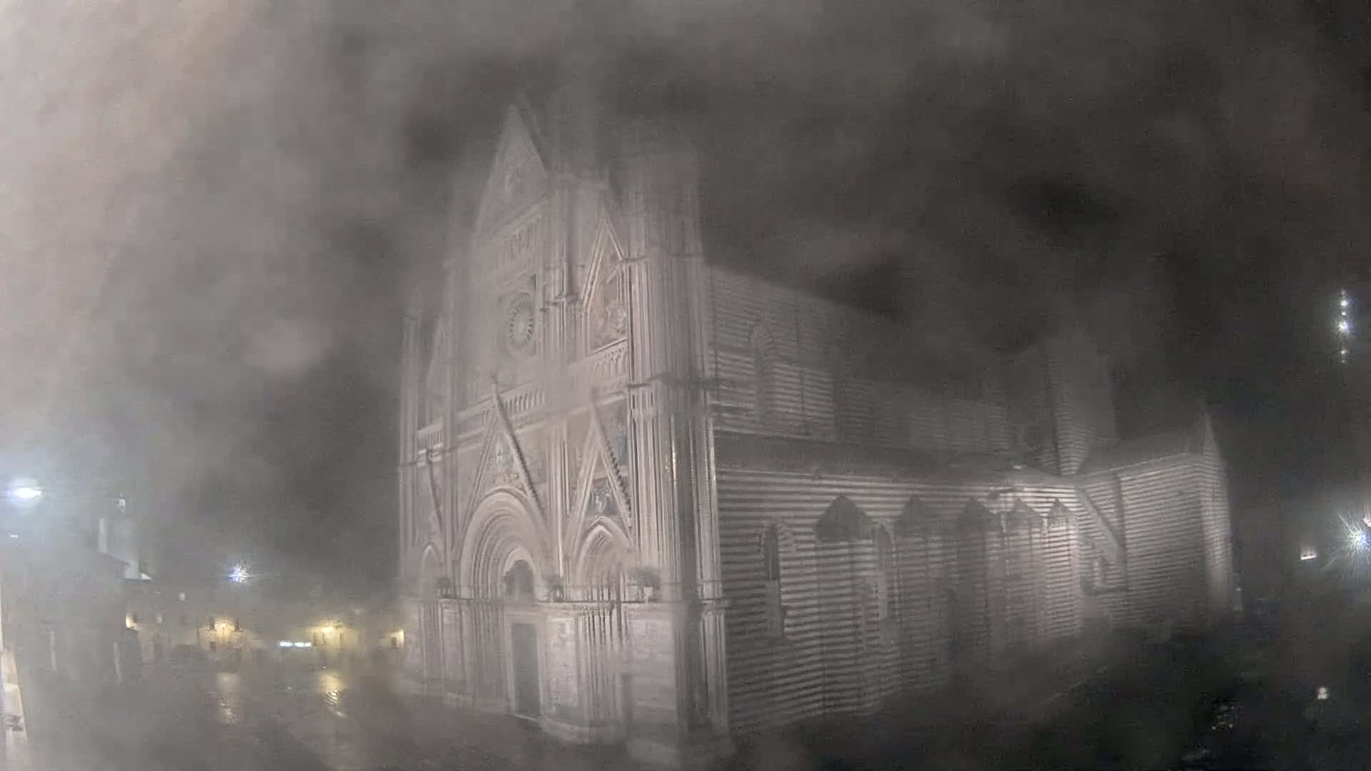 A large, ornate stone cathedral is seen at night in heavy fog or rain.