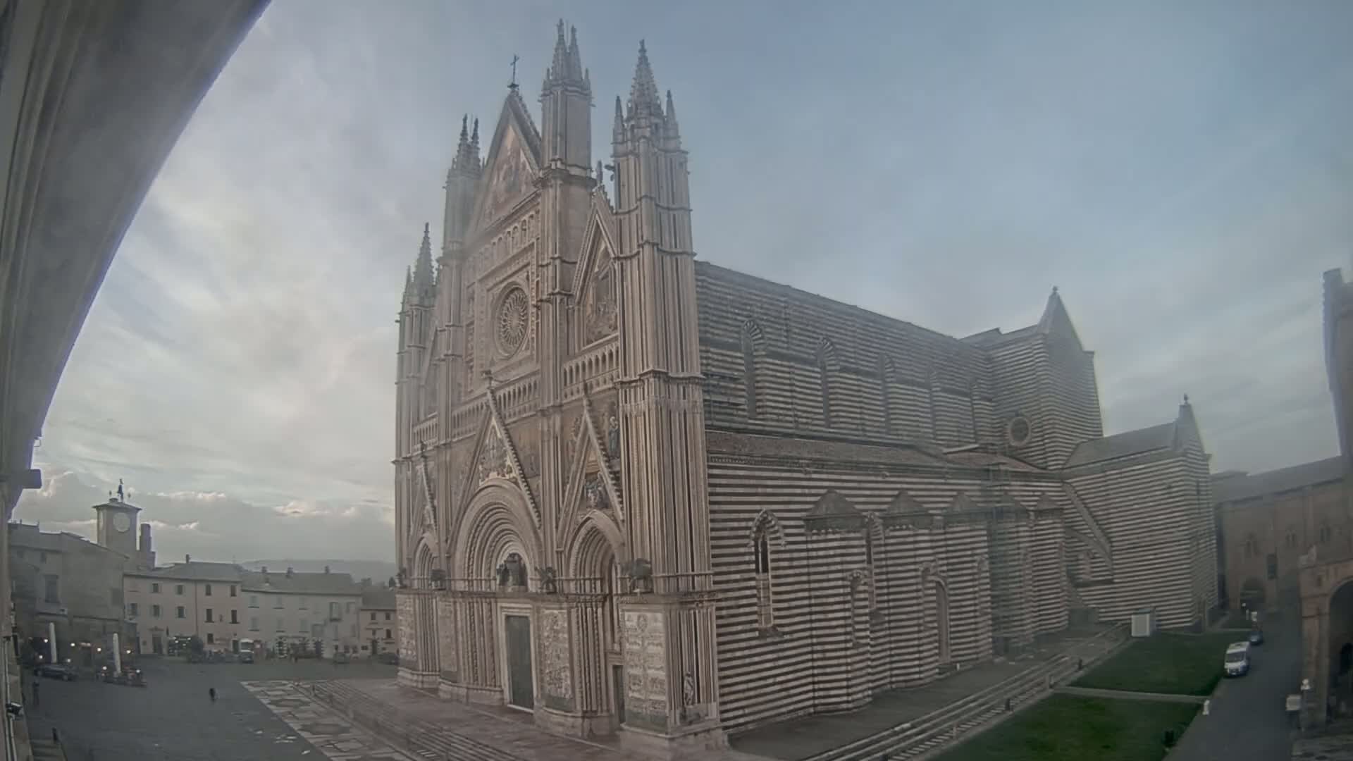 A large, striped cathedral stands in a town square on an overcast day.