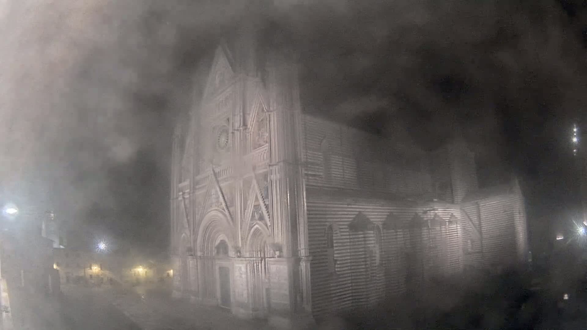 A large, ornate stone church is partially obscured by heavy fog at night.
