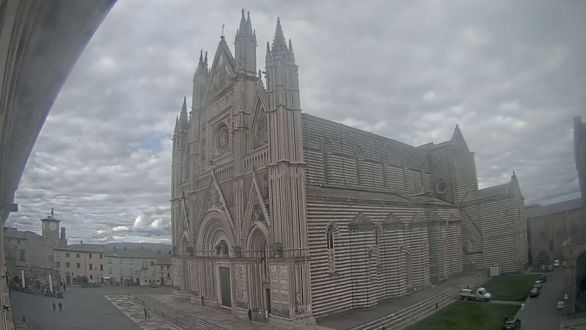 A large, striped cathedral stands in a town square under a cloudy sky.