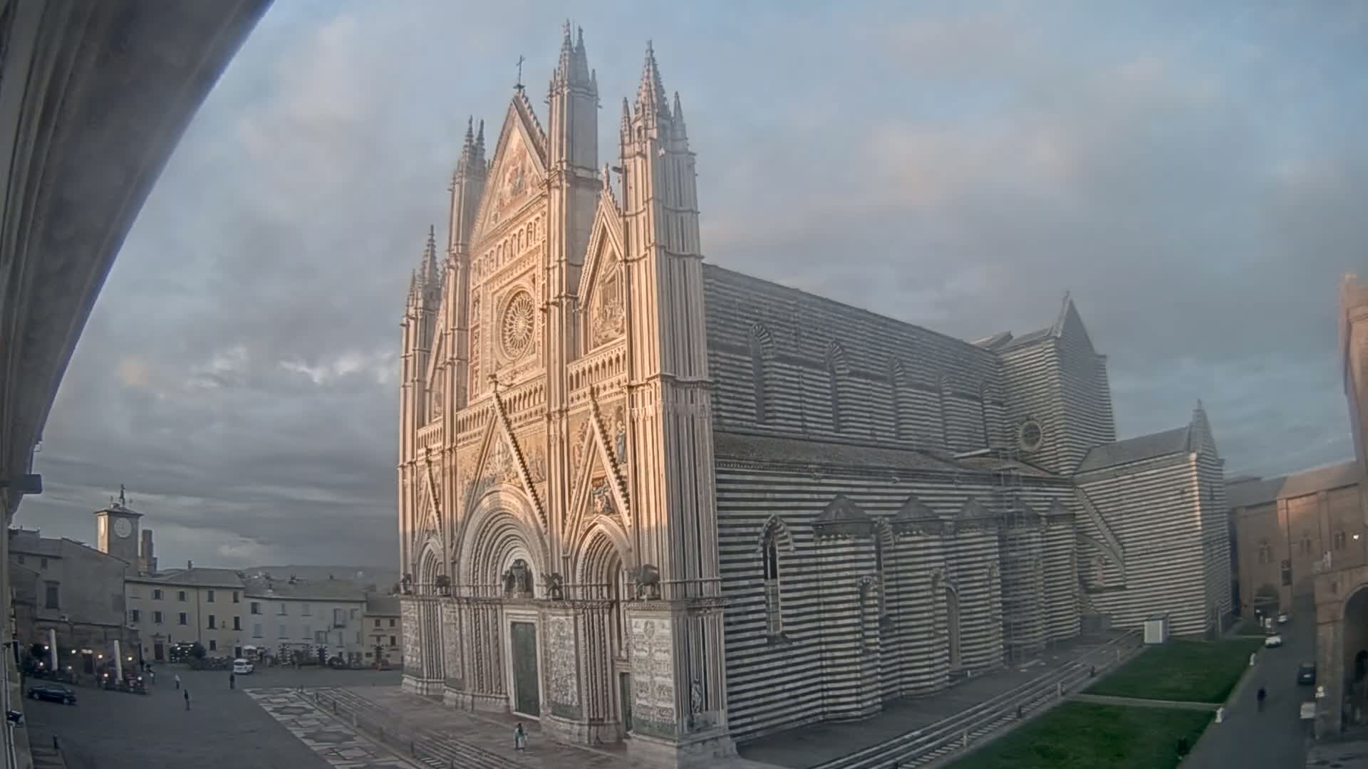A large, striped cathedral stands in a town square under a cloudy sky.
