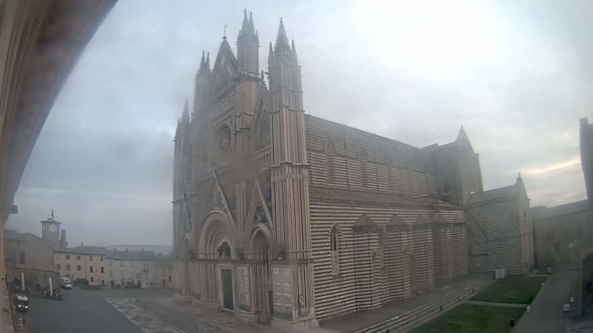 A large, striped stone cathedral stands in a town square on a foggy day.