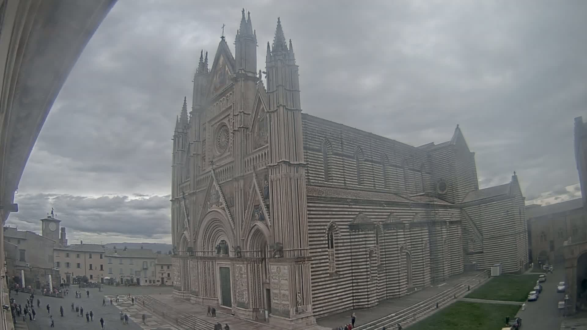 A large, striped cathedral stands in a town square on an overcast day.