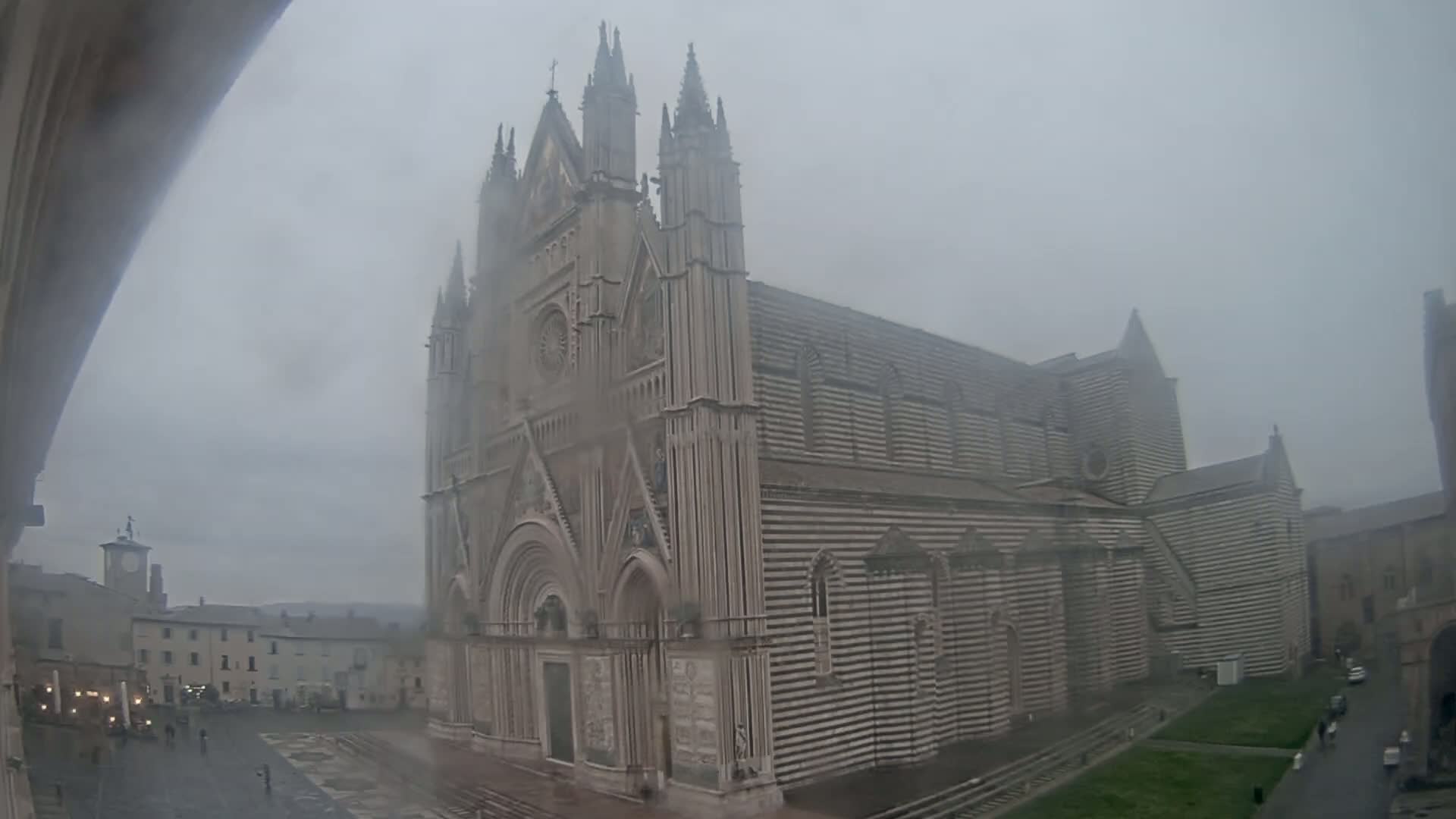 A large, striped cathedral stands in a town square on a foggy day.