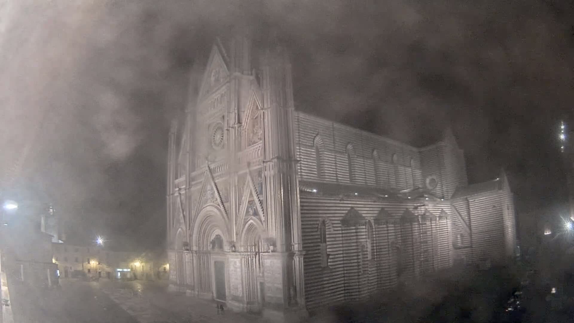 A large, striped stone cathedral is shrouded in thick fog at night.