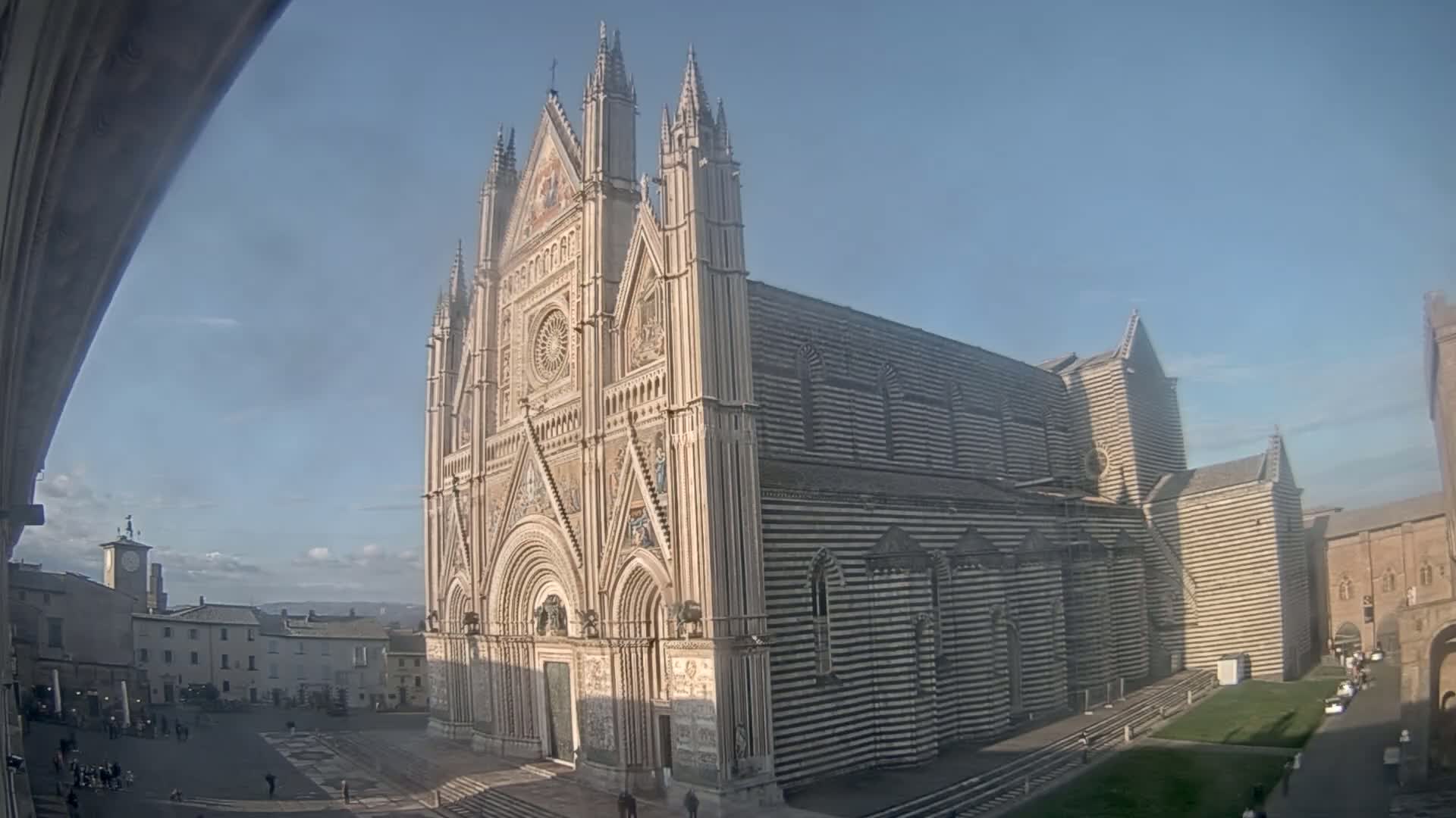 A large, striped cathedral stands in a town square on a sunny day.