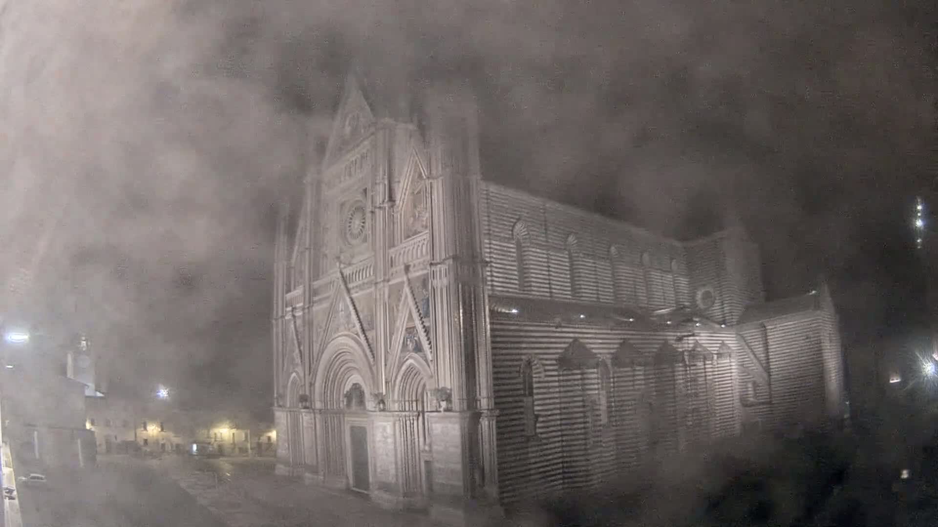 A large, ornate stone cathedral is partially obscured by thick fog at night.