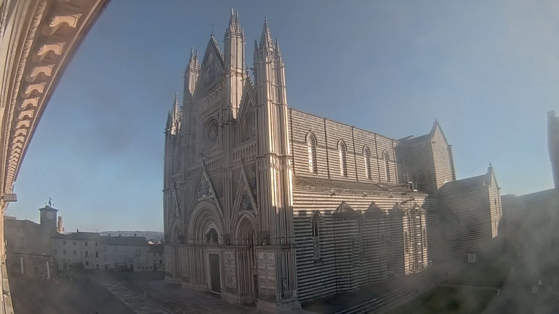 A large striped cathedral stands in a town square on a clear, sunny day.