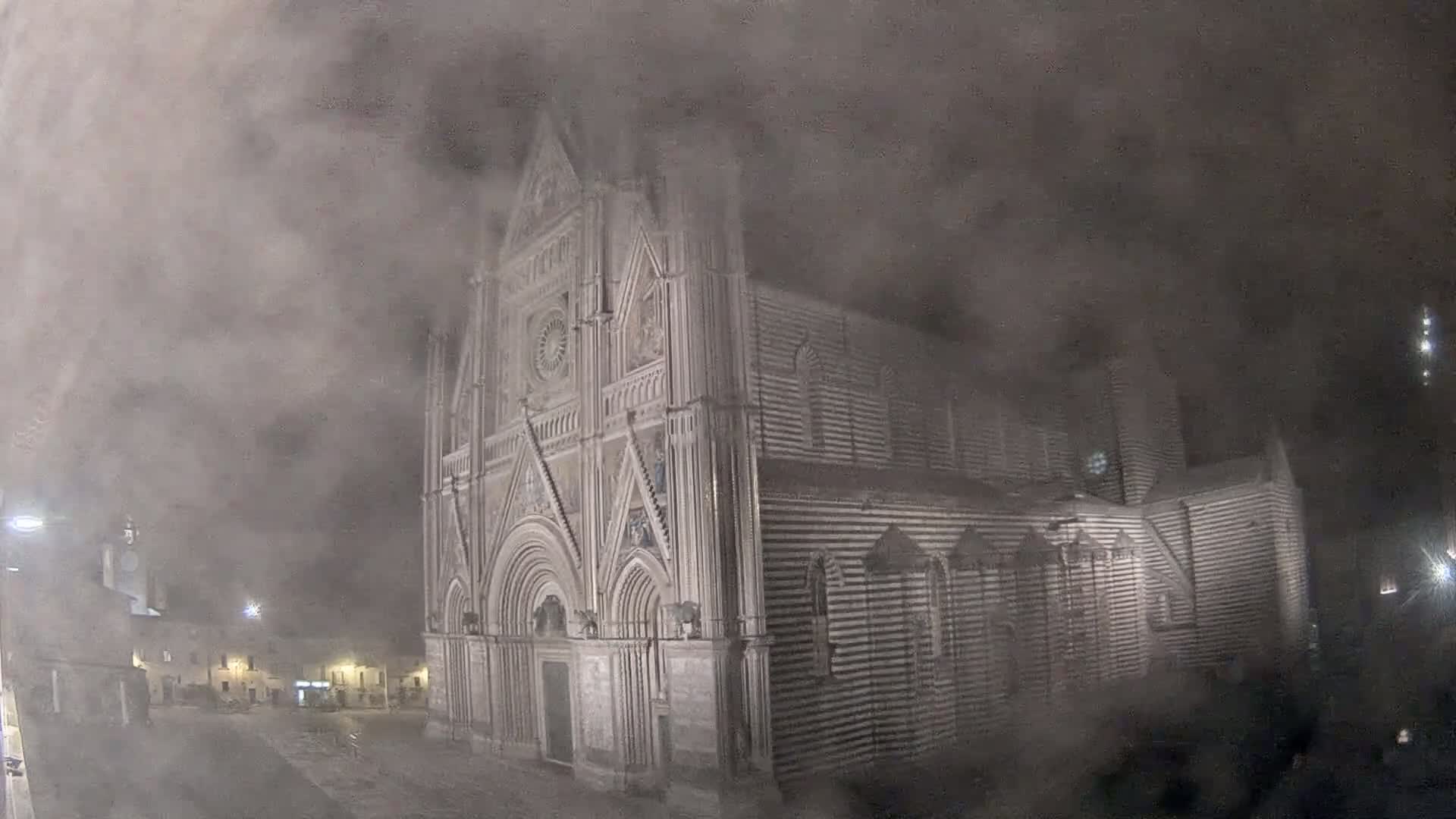 A large, ornate stone cathedral is partially obscured by a thick fog at night.