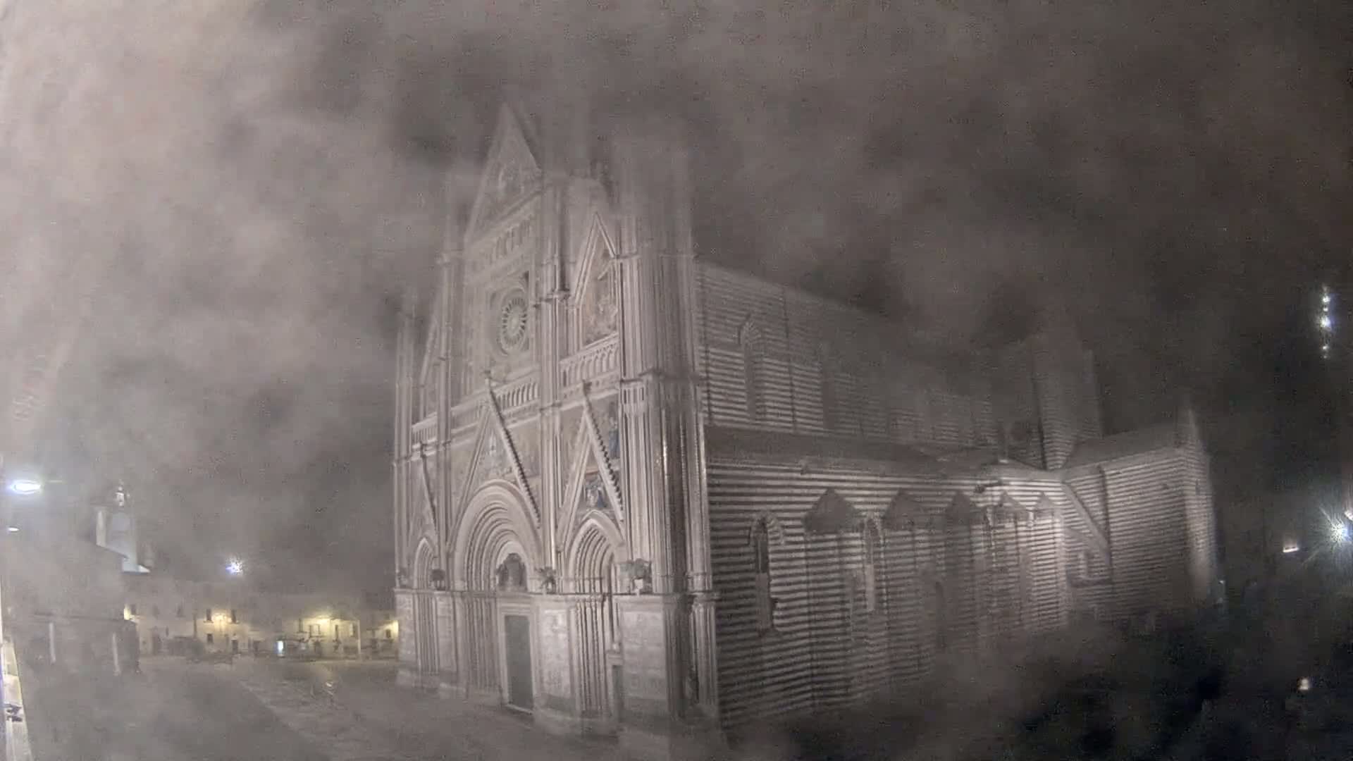 A large, striped cathedral stands in a town square at night, shrouded in thick fog.
