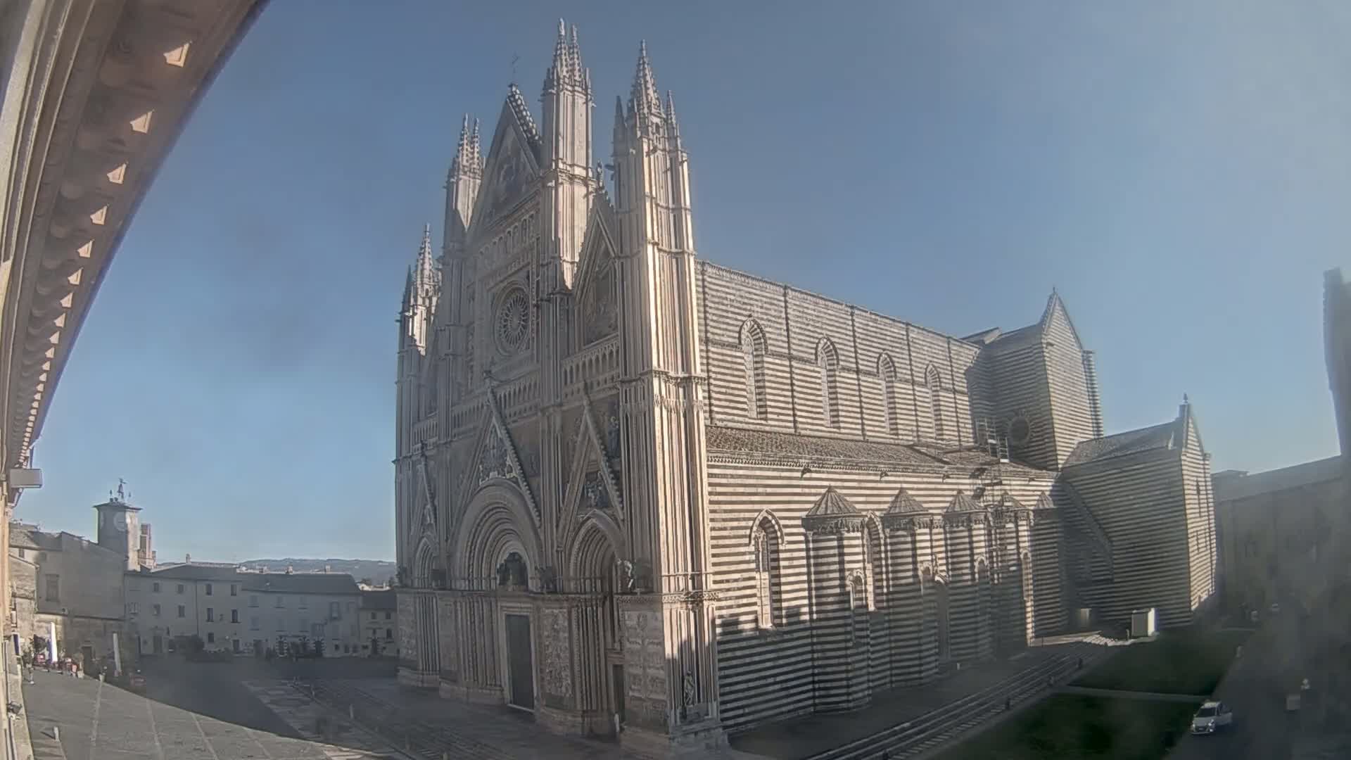 A large, striped cathedral stands in a town square on a sunny day.