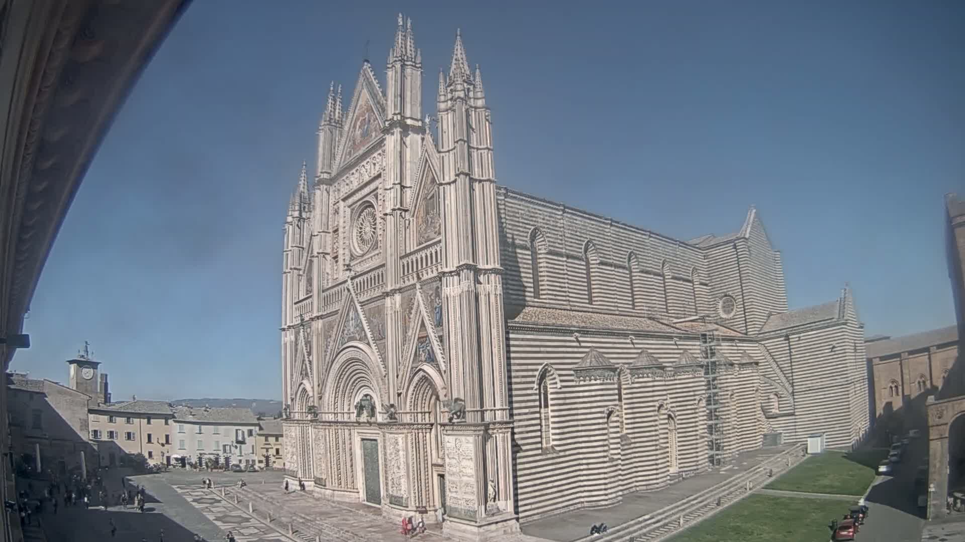 A large, ornate cathedral with black and white striped exterior walls stands in a sunny plaza, surrounded by smaller buildings.