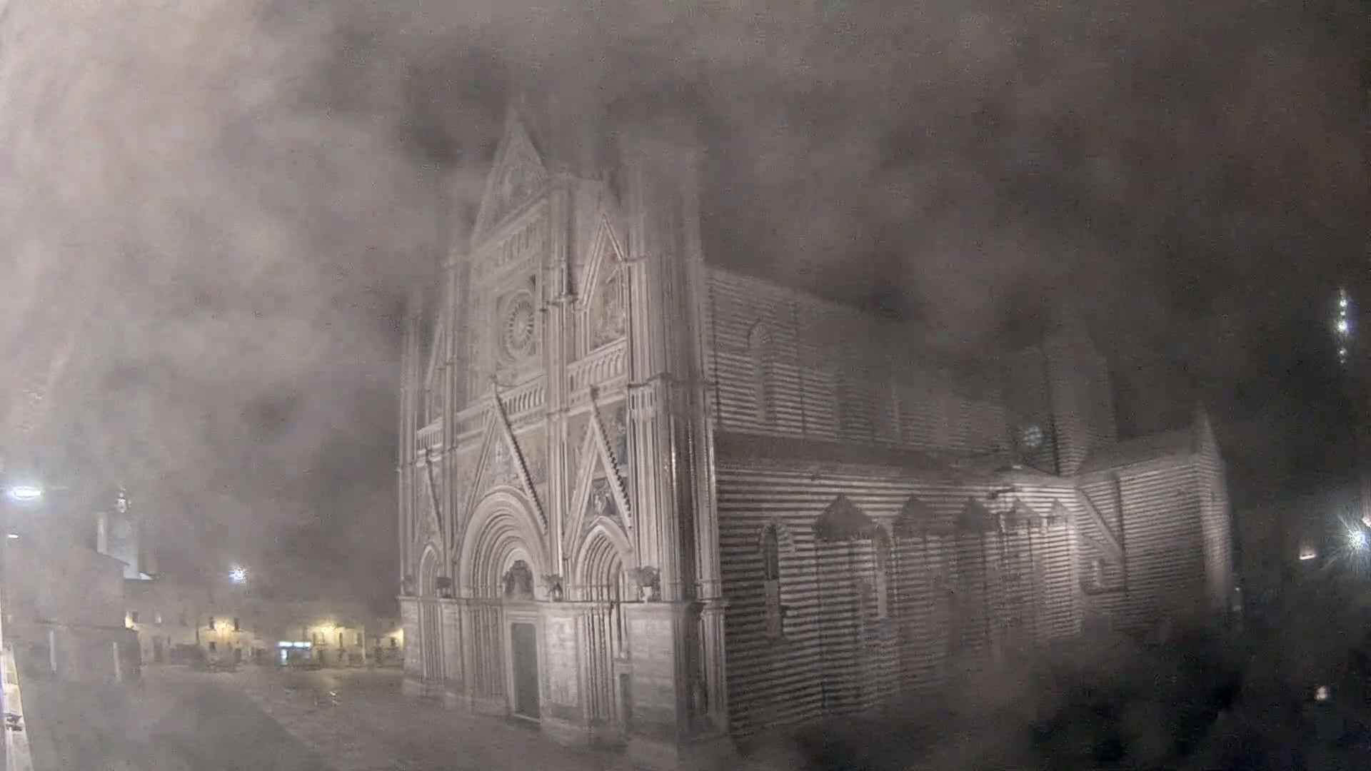 A large, ornate stone cathedral is partially obscured by a thick fog at night.