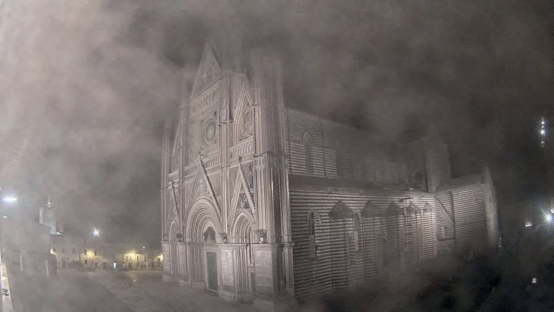 A large, ornate stone cathedral is partially obscured by thick fog at night.