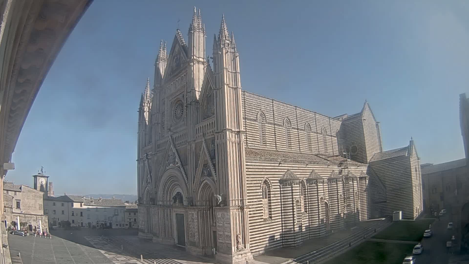 A large, striped cathedral stands in a town square on a sunny day.