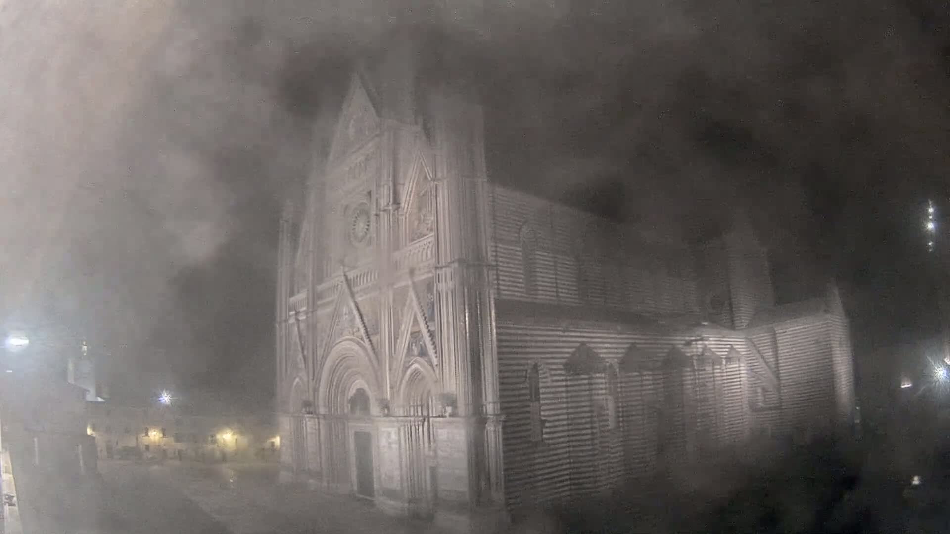 A large, ornate stone cathedral is partially obscured by heavy fog at night.