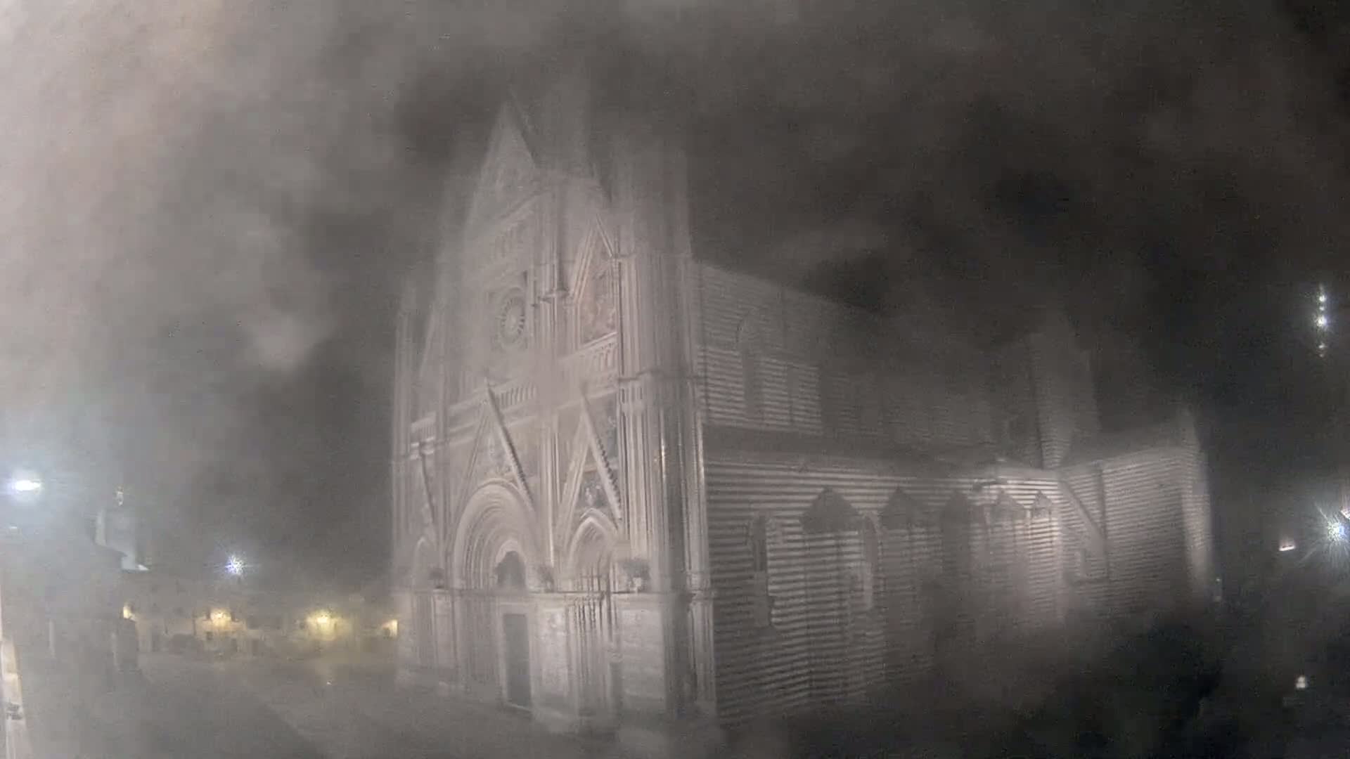 A large, ornate stone building, possibly a cathedral, is partially obscured by a heavy fog at night.