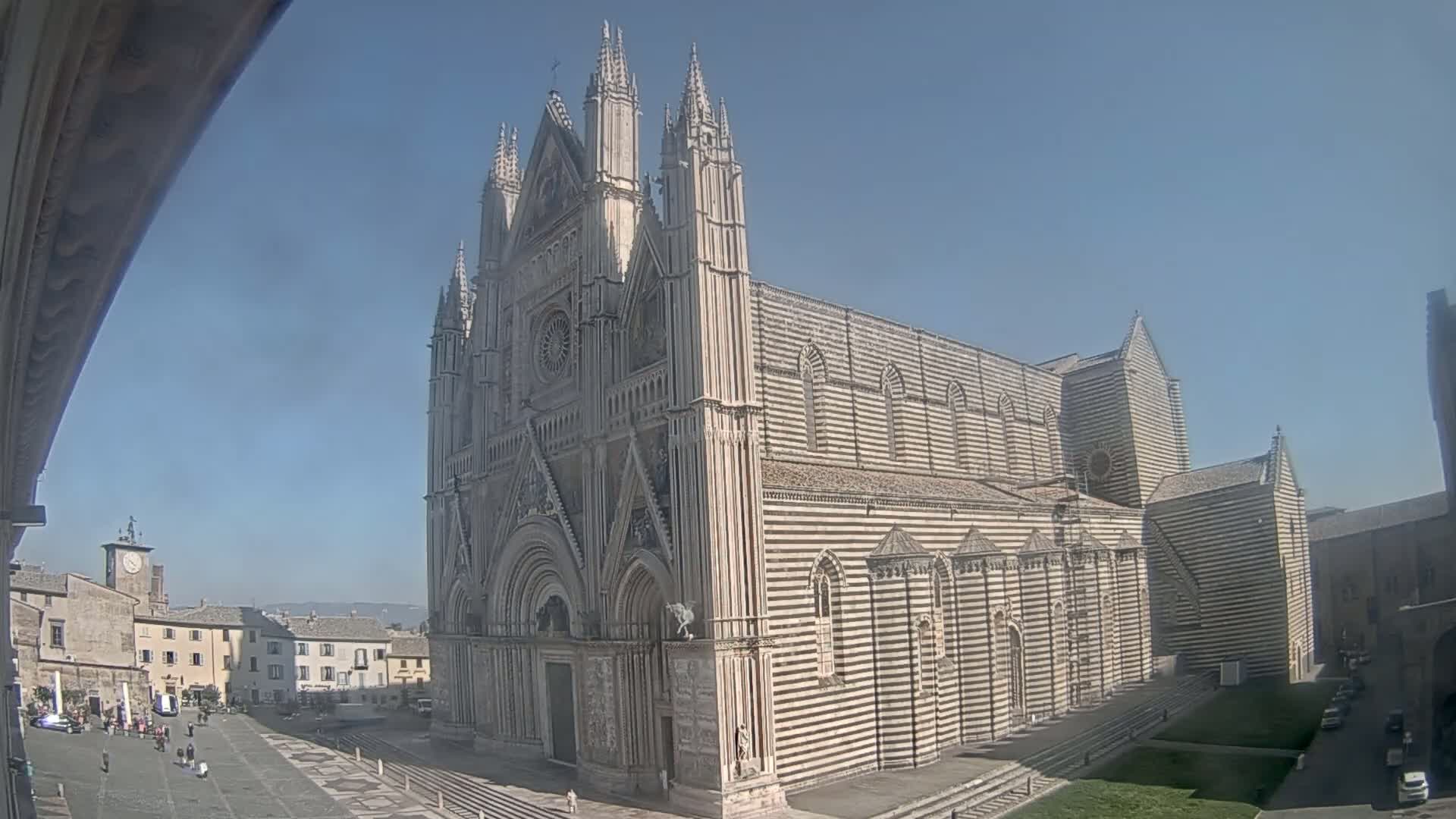 A large striped cathedral stands in a town square on a sunny day.