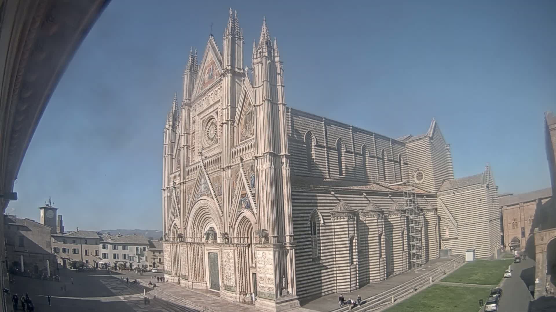 A large, ornate cathedral with black and white striped exterior stands in a sunny square.