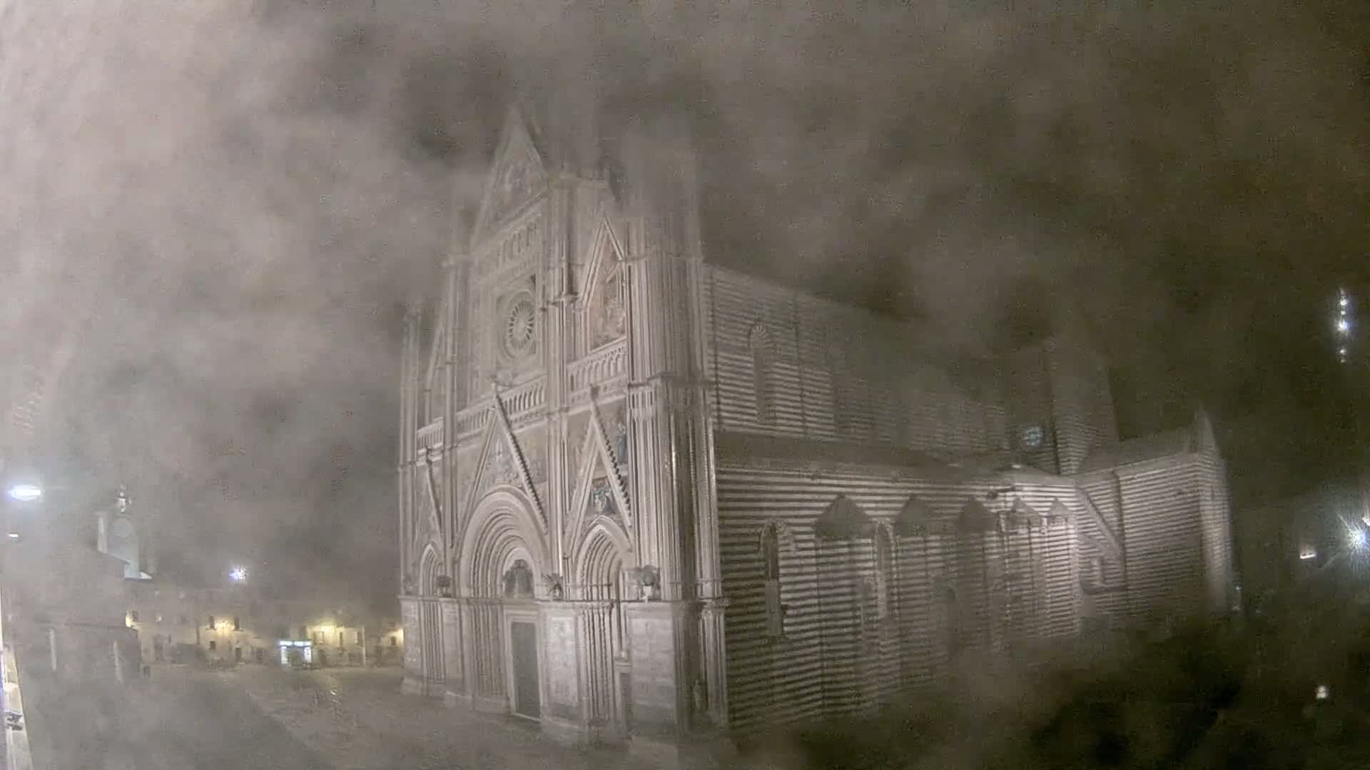 A large, striped stone cathedral is partially obscured by heavy fog at night.