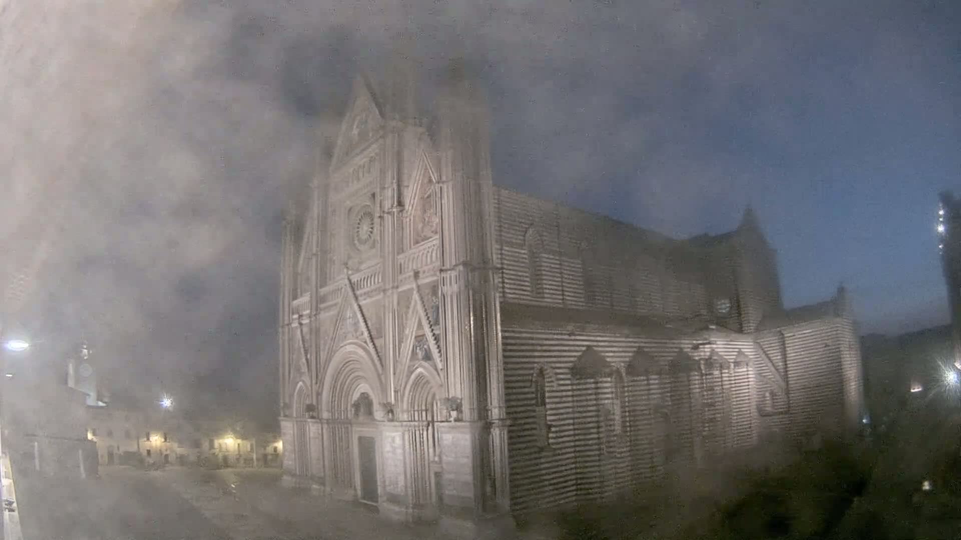 A large, striped stone cathedral is partially obscured by fog at night.