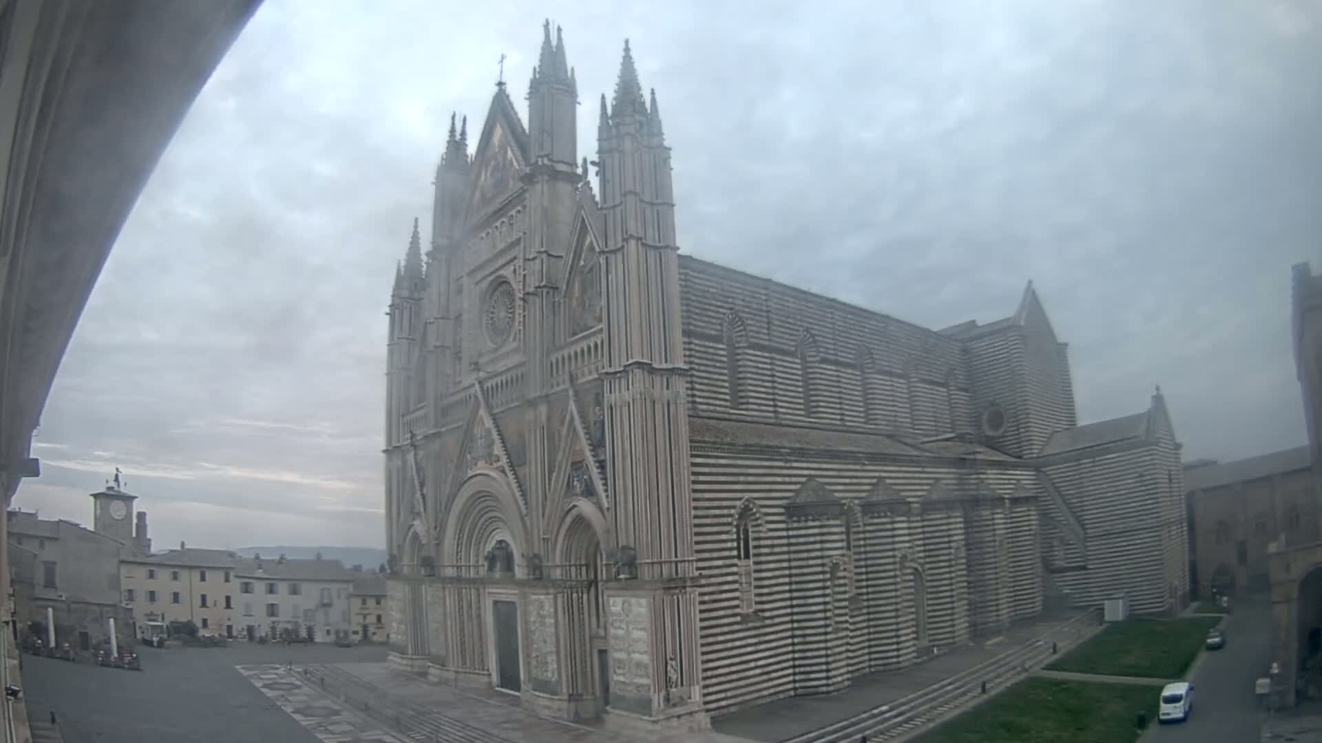 A large, striped stone cathedral stands in a town square on an overcast day.