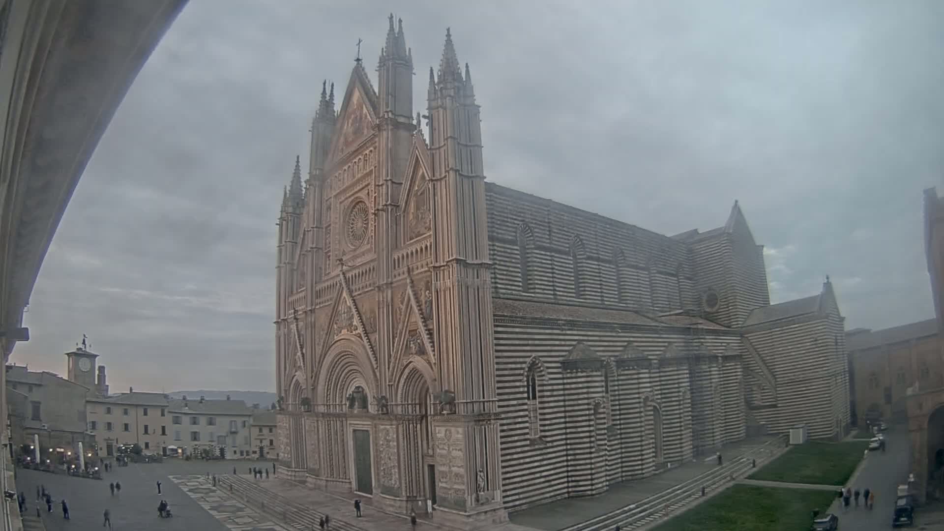 A large, striped cathedral stands in a town square on an overcast day.