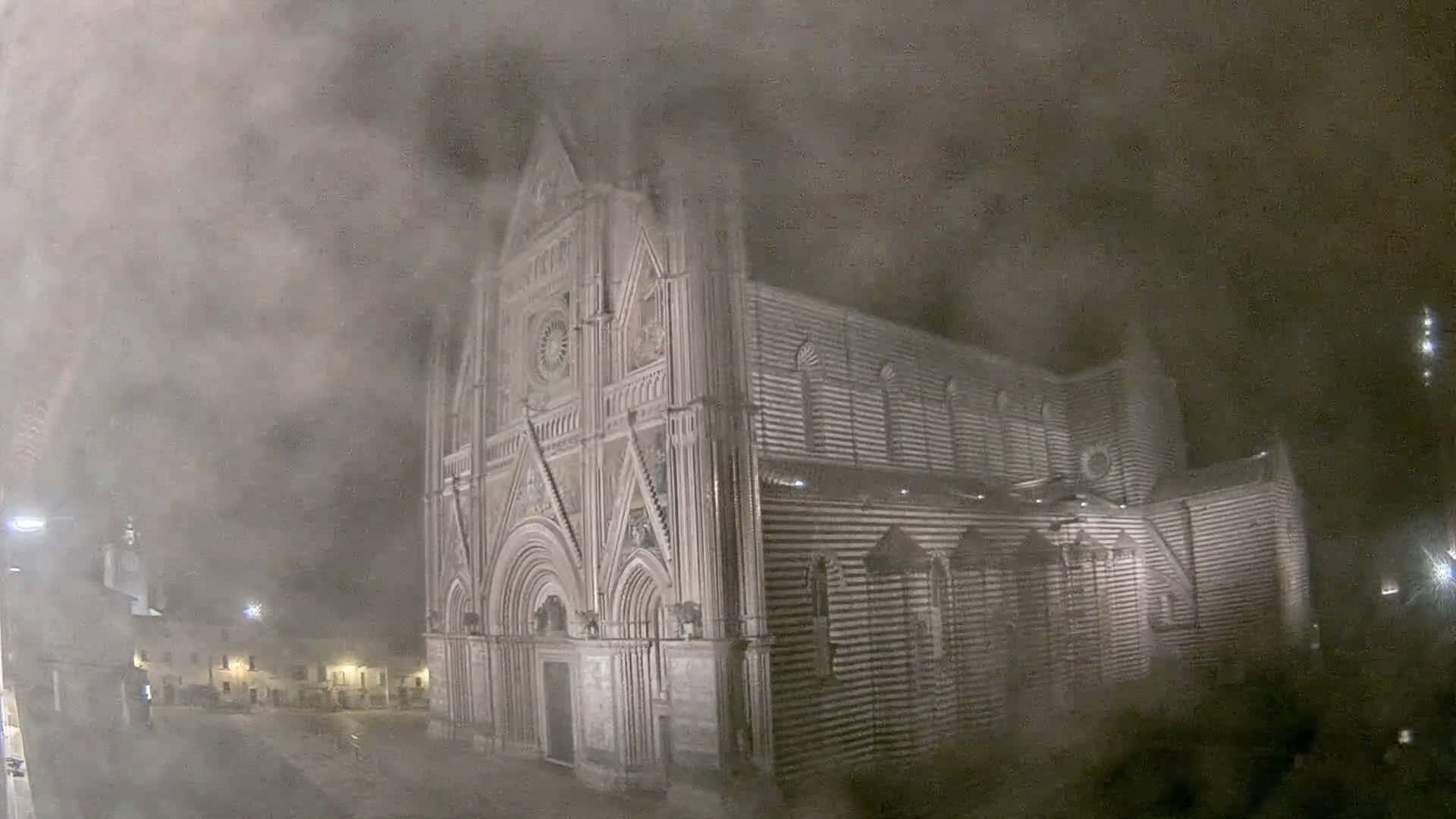 A large, striped stone cathedral stands at night, shrouded in a thick fog.