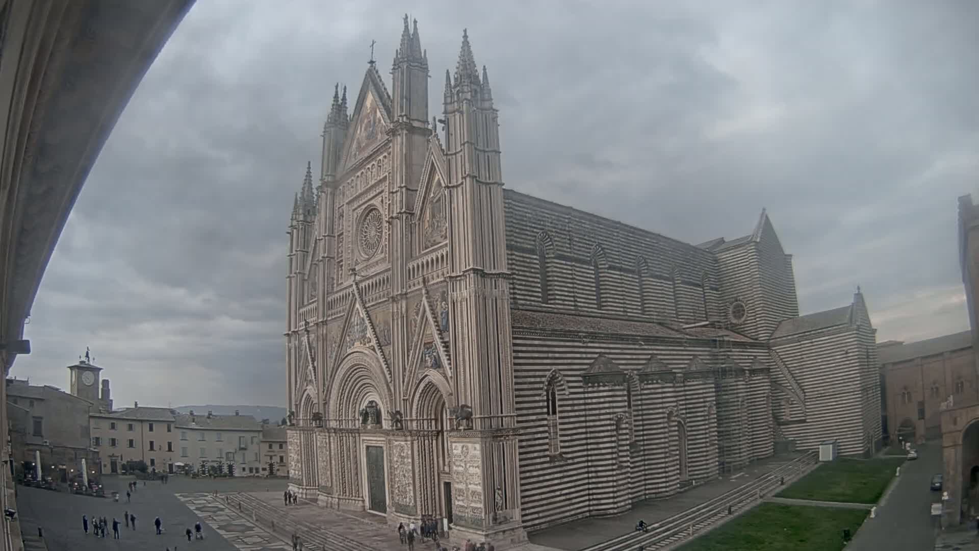 A large, striped cathedral stands in a town square under a cloudy sky.