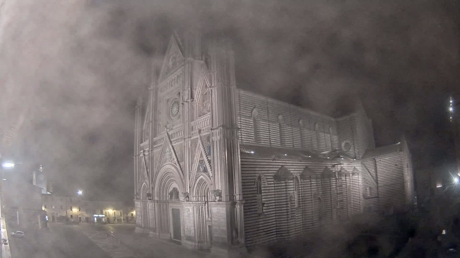 A large, striped cathedral stands in a town square at night, obscured by heavy fog.