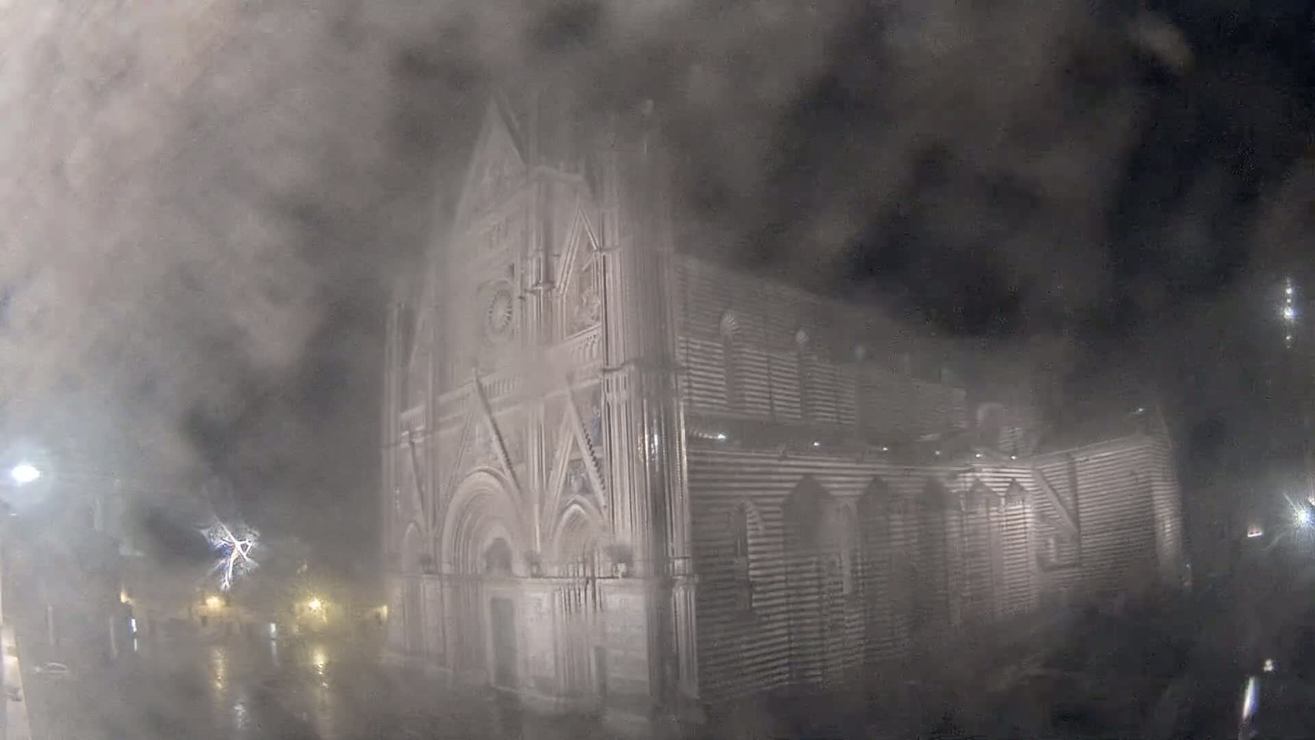 A large stone cathedral is partially obscured by heavy fog and rain at night.
