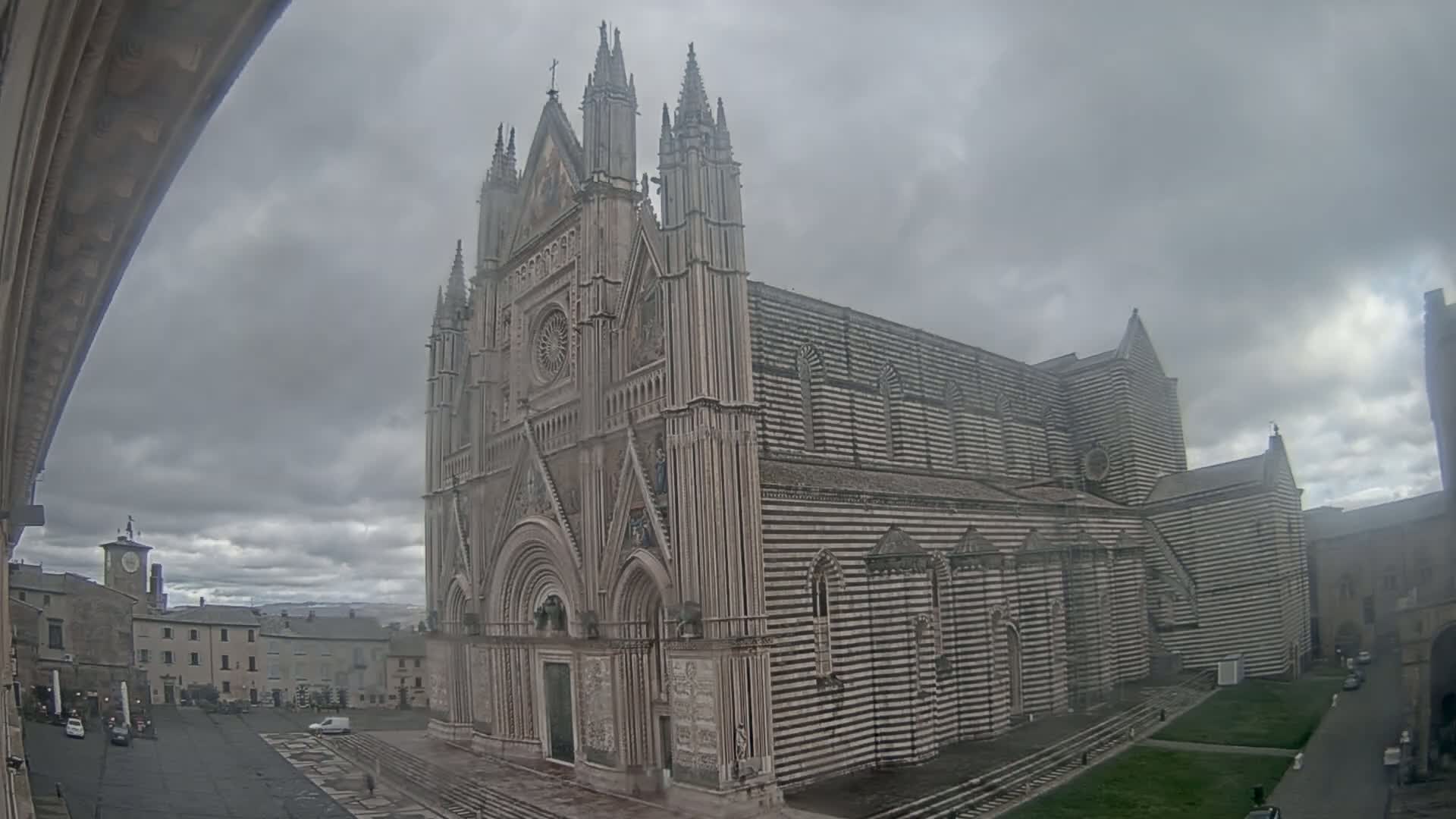 A large, striped cathedral stands in a town square under a cloudy sky.