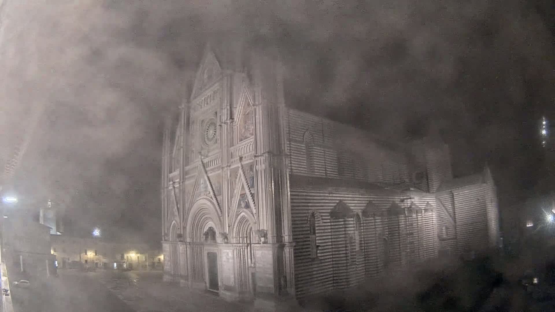 A large, ornate cathedral stands at night in heavy fog or mist.