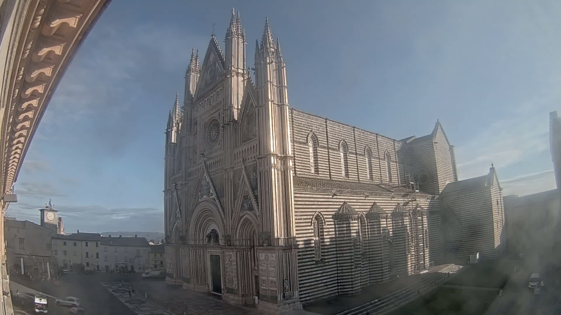 A large, striped cathedral stands in a town square on a partly sunny day.