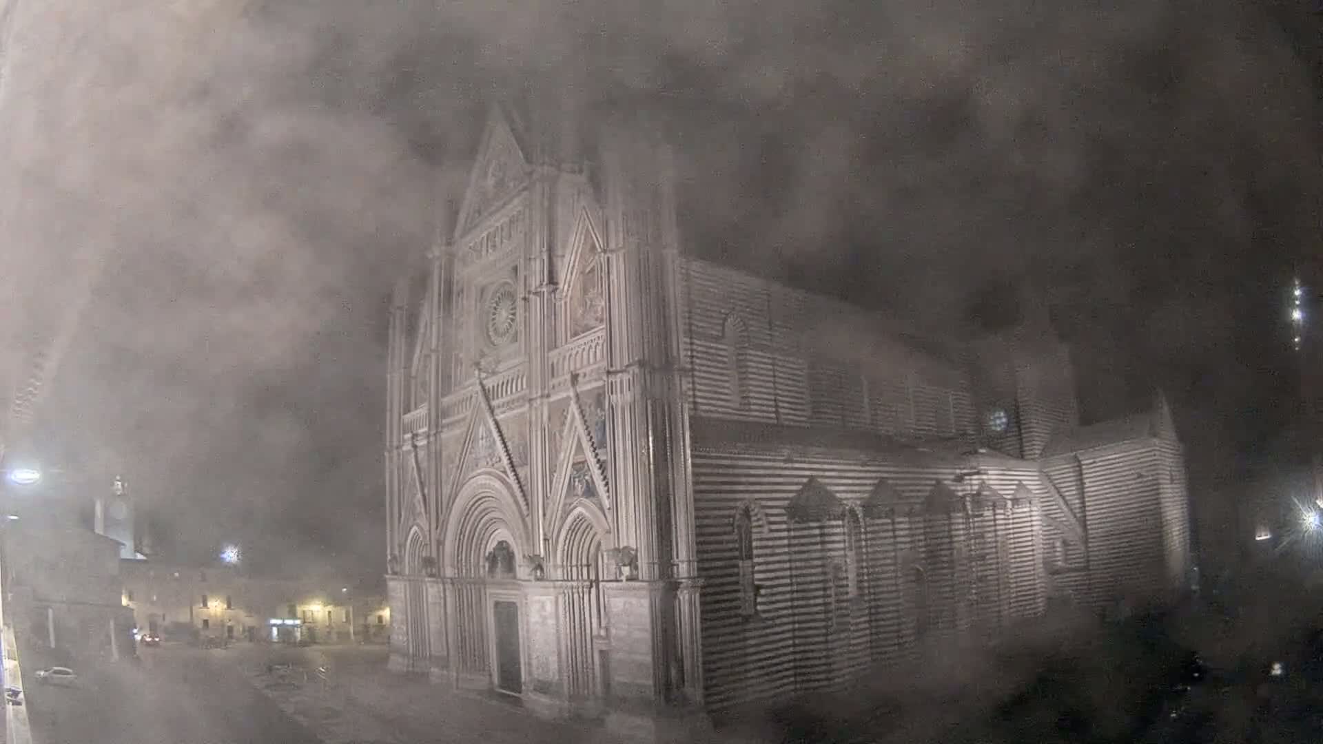 A large, striped stone cathedral stands at night in a thick fog.