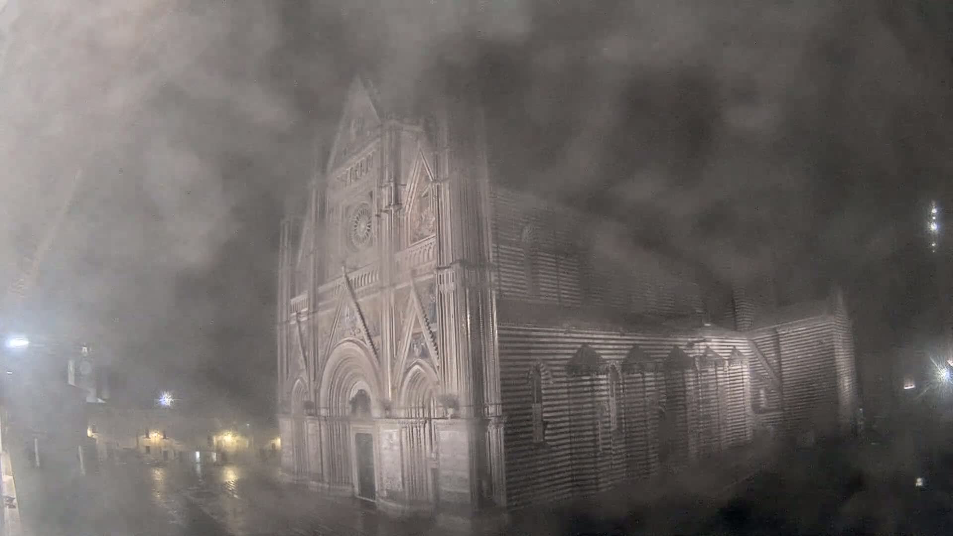 A large stone cathedral is partially obscured by heavy fog or mist at night.